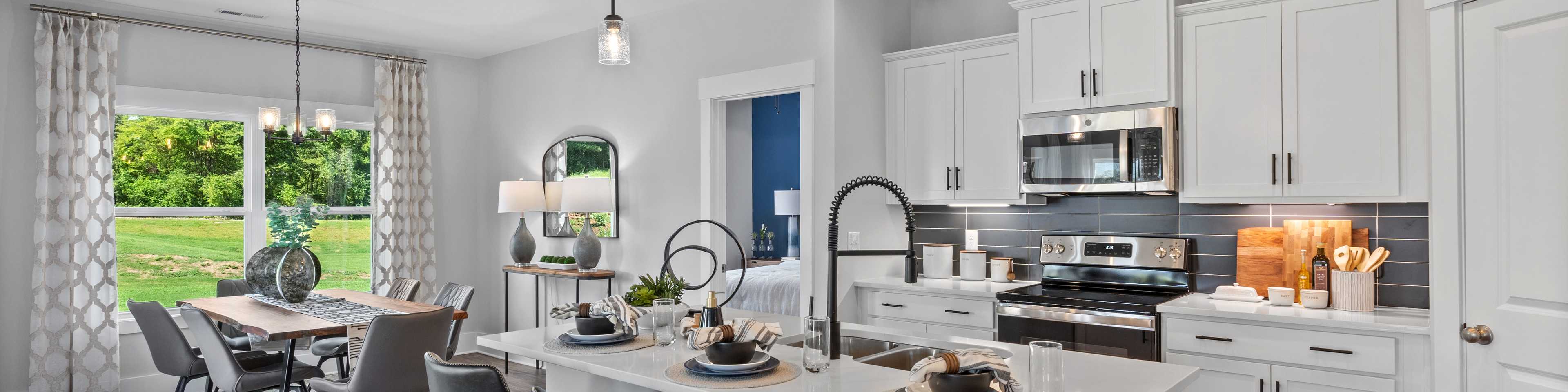 Spacious modern kitchen in new Arab home with white cabinets, large island, bar stools, and dining nook overlooking greenery