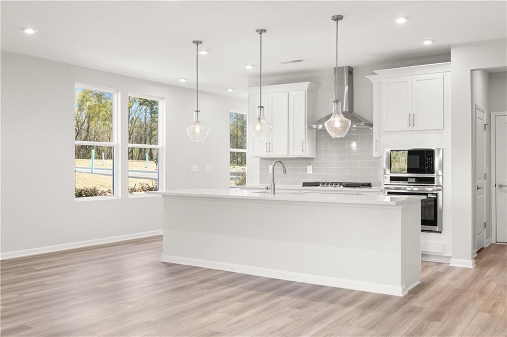 Bright white kitchen with island, stainless steel appliances, subway tile backsplash, and pendant lights in Davidson Homes The Cary A, Winder, GA