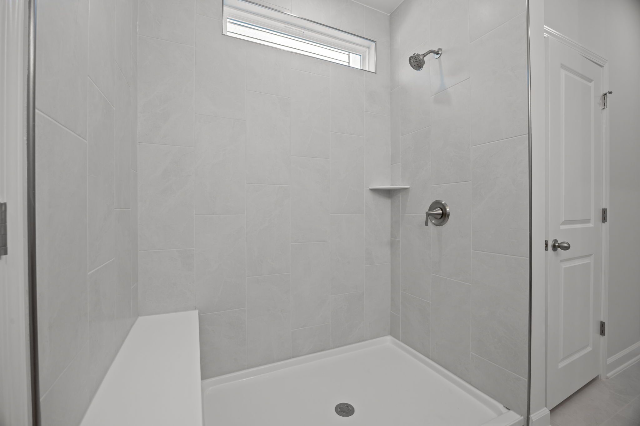 Modern walk-in shower with tiled walls and built-in bench in the master suite of The Ashport B home design.