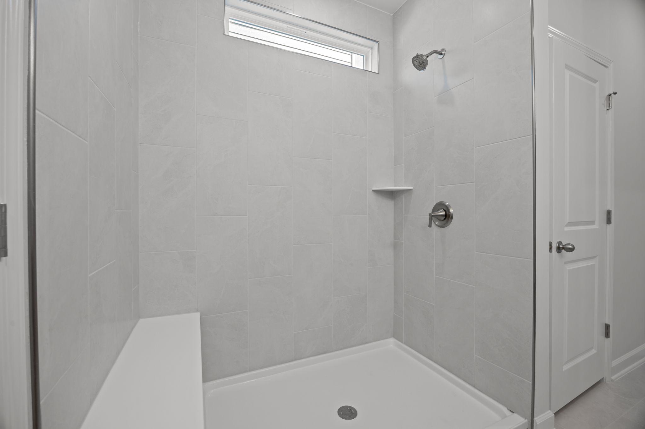 Modern walk-in shower with tiled walls and built-in bench in the master suite of The Ashport B home design.
