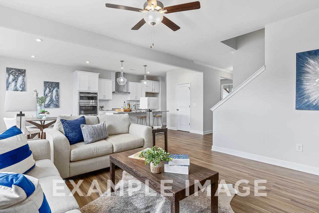 Spacious open-concept living room and kitchen in The Willow C with white cabinetry, island, neutral sofa, and hardwood floors