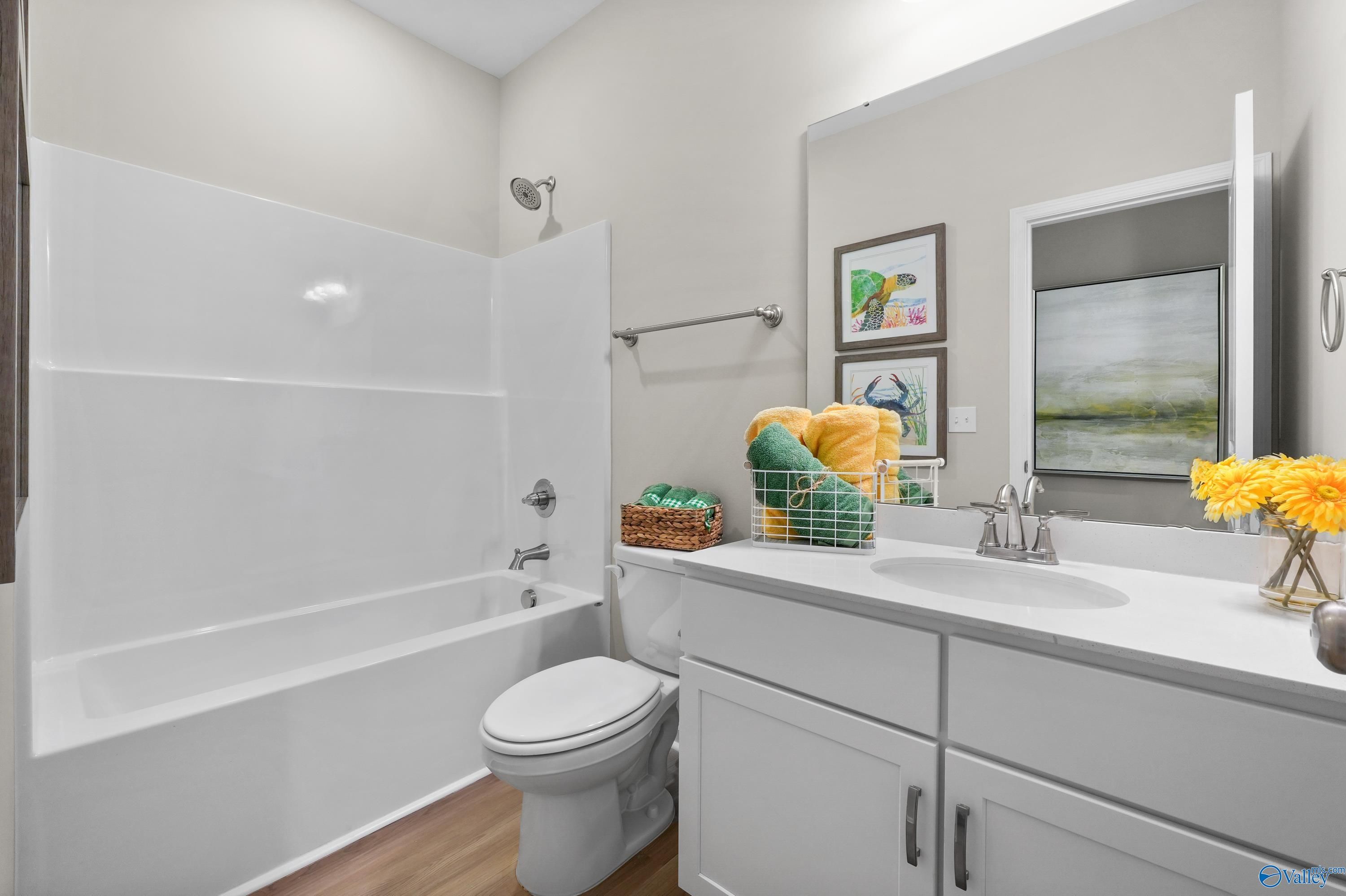 Modern bathroom with white tub-shower combo, vanity sink, and decorative yellow flowers in The Malibu home, Madison, Alabama