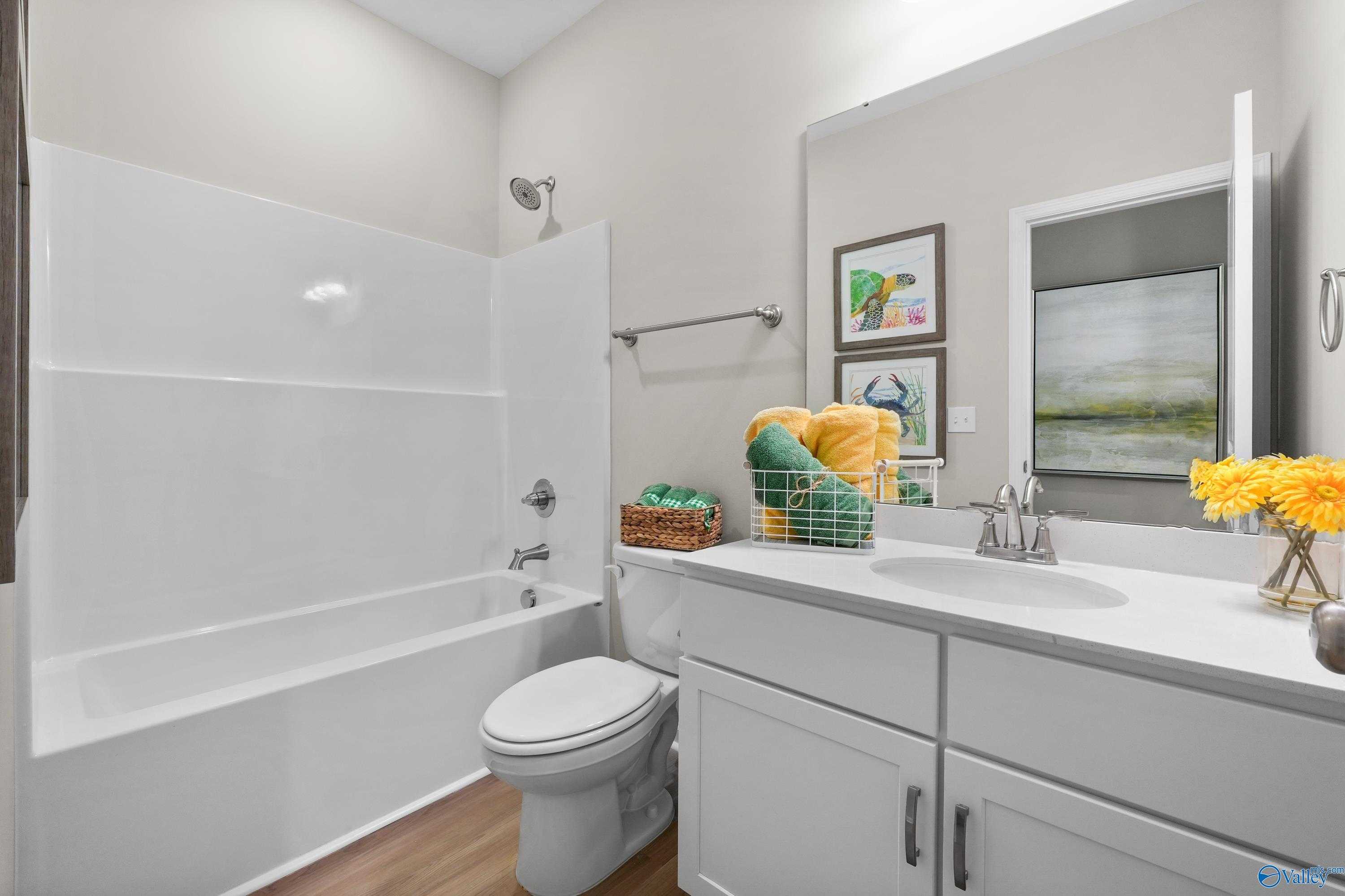 Modern bathroom with white tub-shower combo, vanity sink, and decorative yellow flowers in The Malibu home, Madison, Alabama