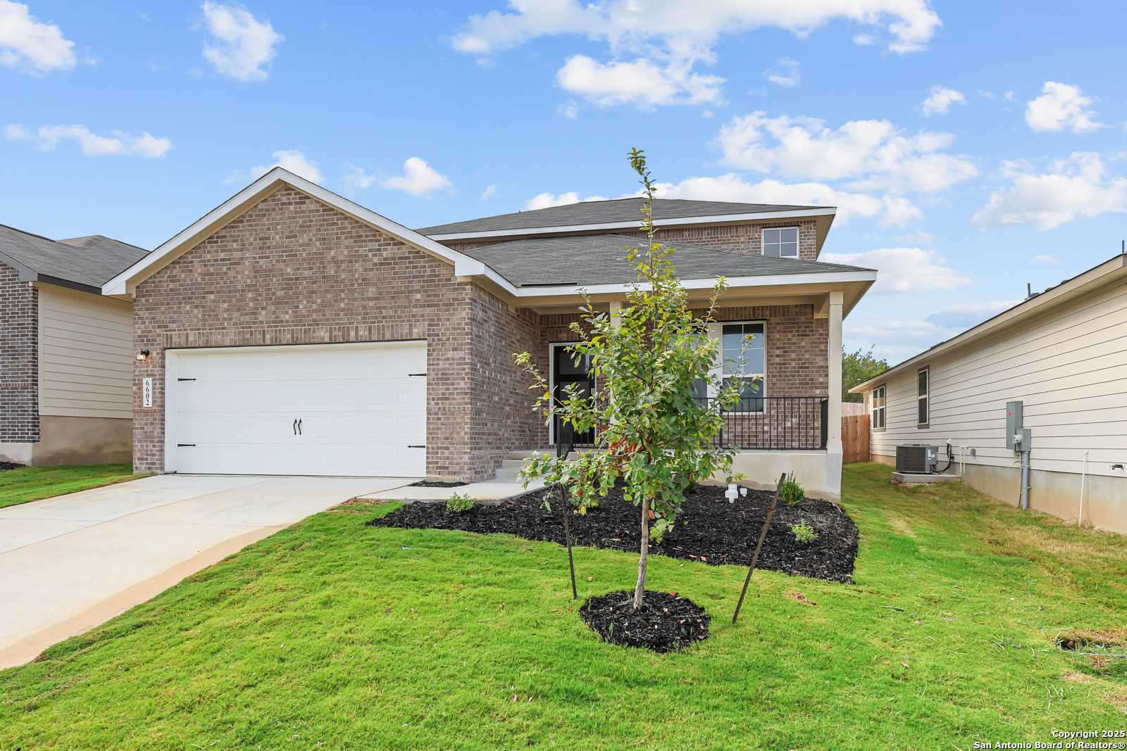 Modern two-story brick home with 2-car garage, front lawn, and young tree in Royal Crest, San Antonio, Texas
