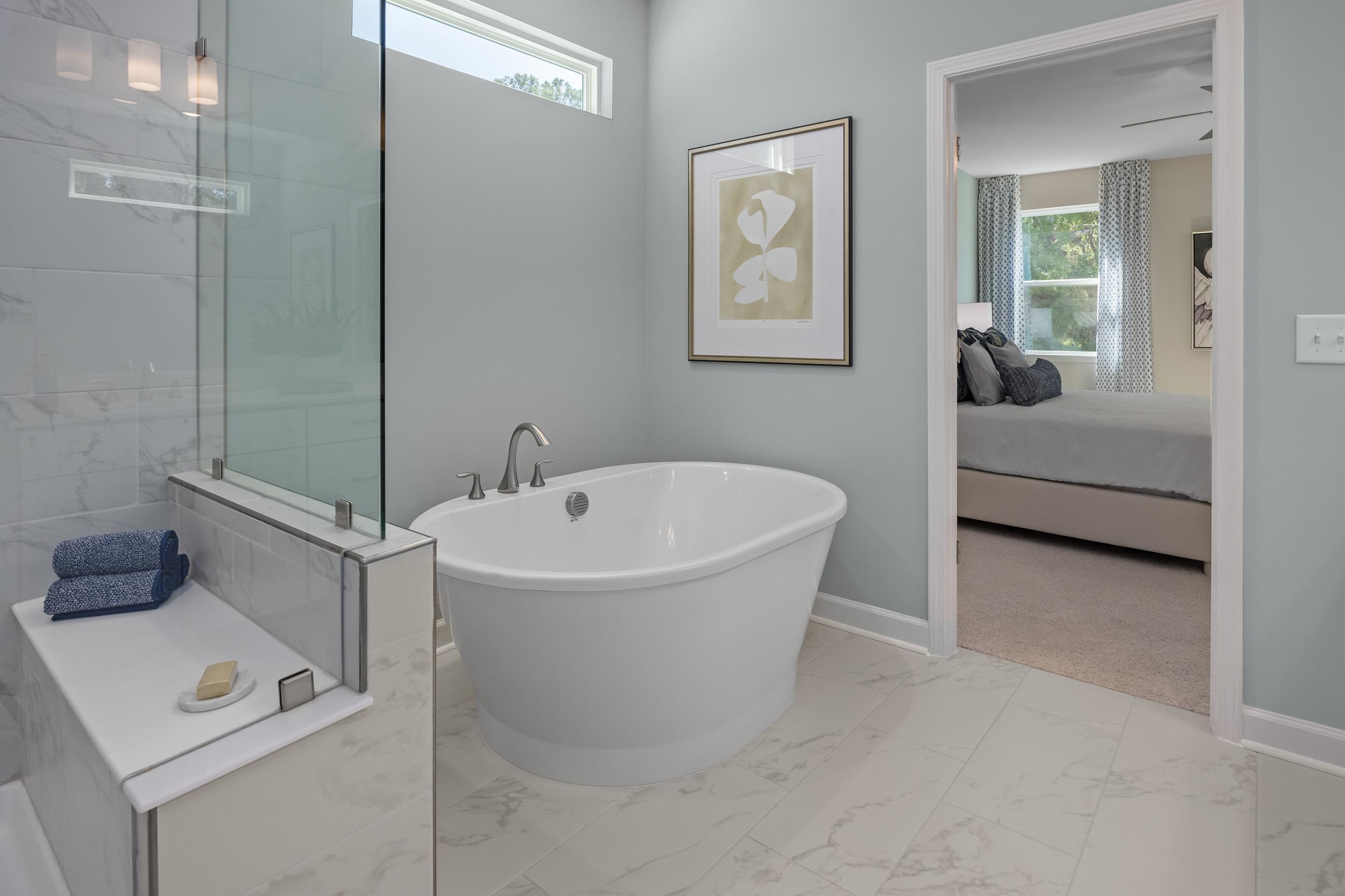 Spacious master bathroom in The Hickory II with freestanding tub, glass shower, and bedroom view