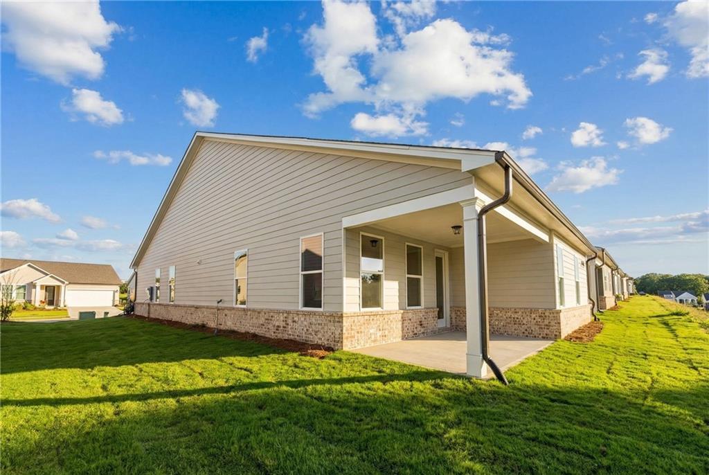 Side view of beige single-story home with covered porch, brick accents, and lush green lawn in Kelly Preserve, Loganville, Georgia