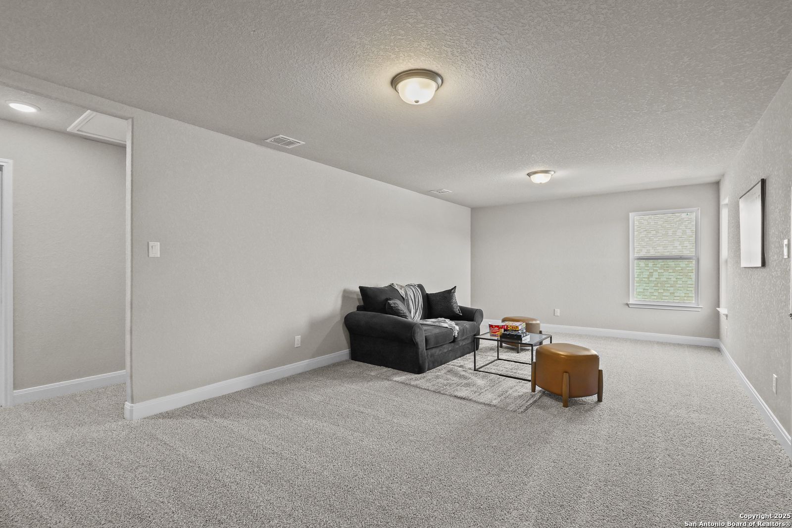 Cozy family room with black leather sofa, coffee table, and neutral gray walls in Davidson Homes The Jennings G, Castroville, Texas