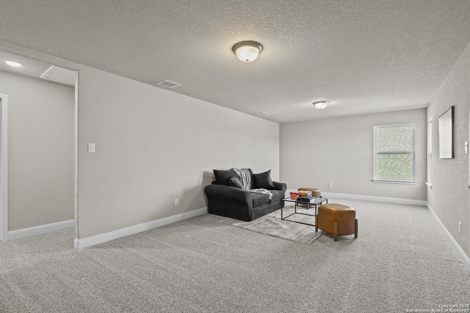 Cozy family room with black leather sofa, coffee table, and neutral gray walls in Davidson Homes The Jennings G, Castroville, Texas