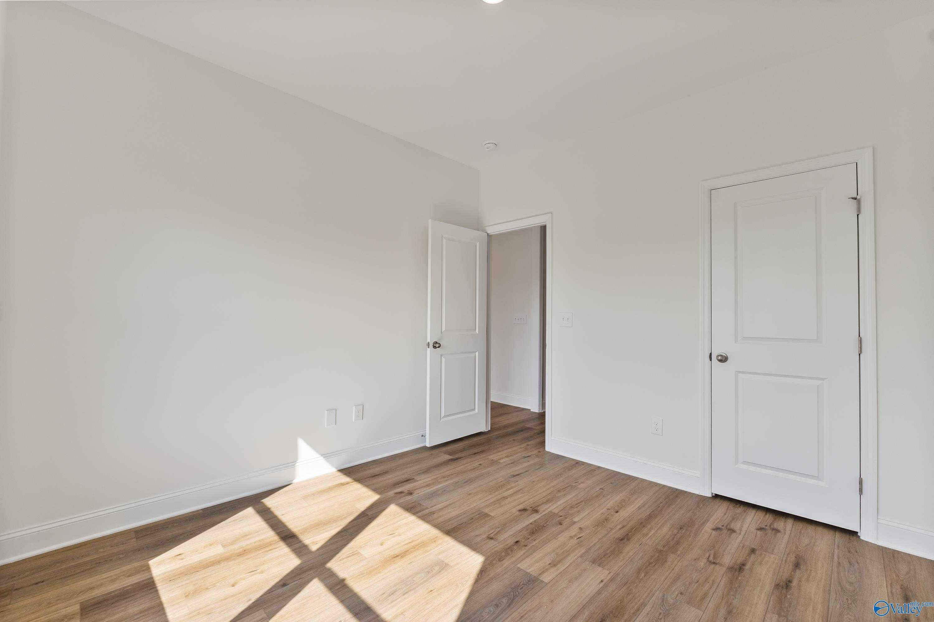 Bright bedroom with light oak hardwood floors, white walls, and double doors in Davidson Homes The Shelby A, New Market, Alabama