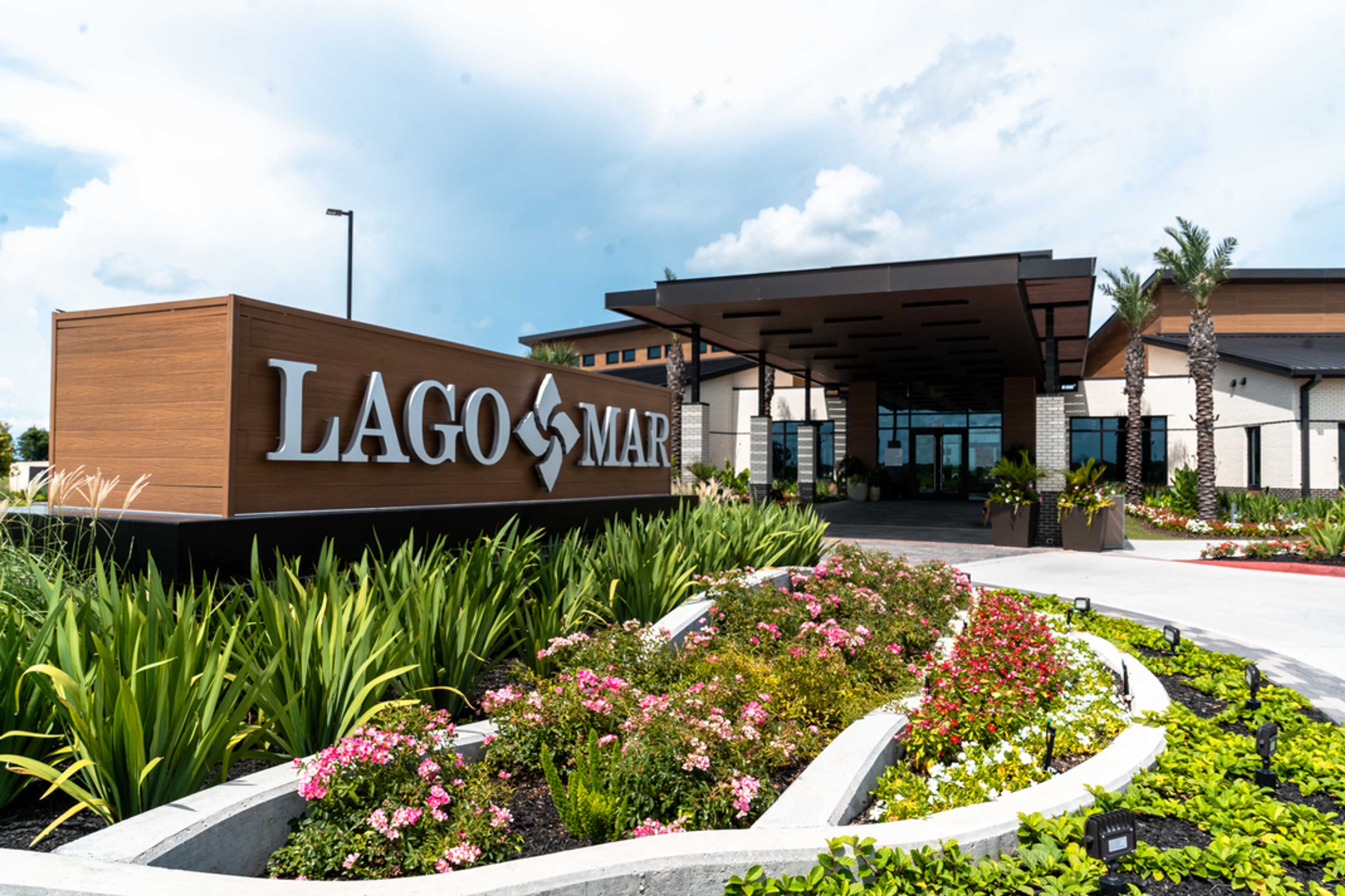 Lago Mar community entrance sign in Texas City Texas with modern covered building, palm trees, and vibrant flower beds