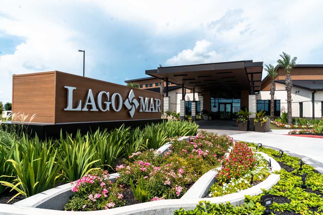 Lago Mar community entrance sign in Texas City Texas with modern covered building, palm trees, and vibrant flower beds