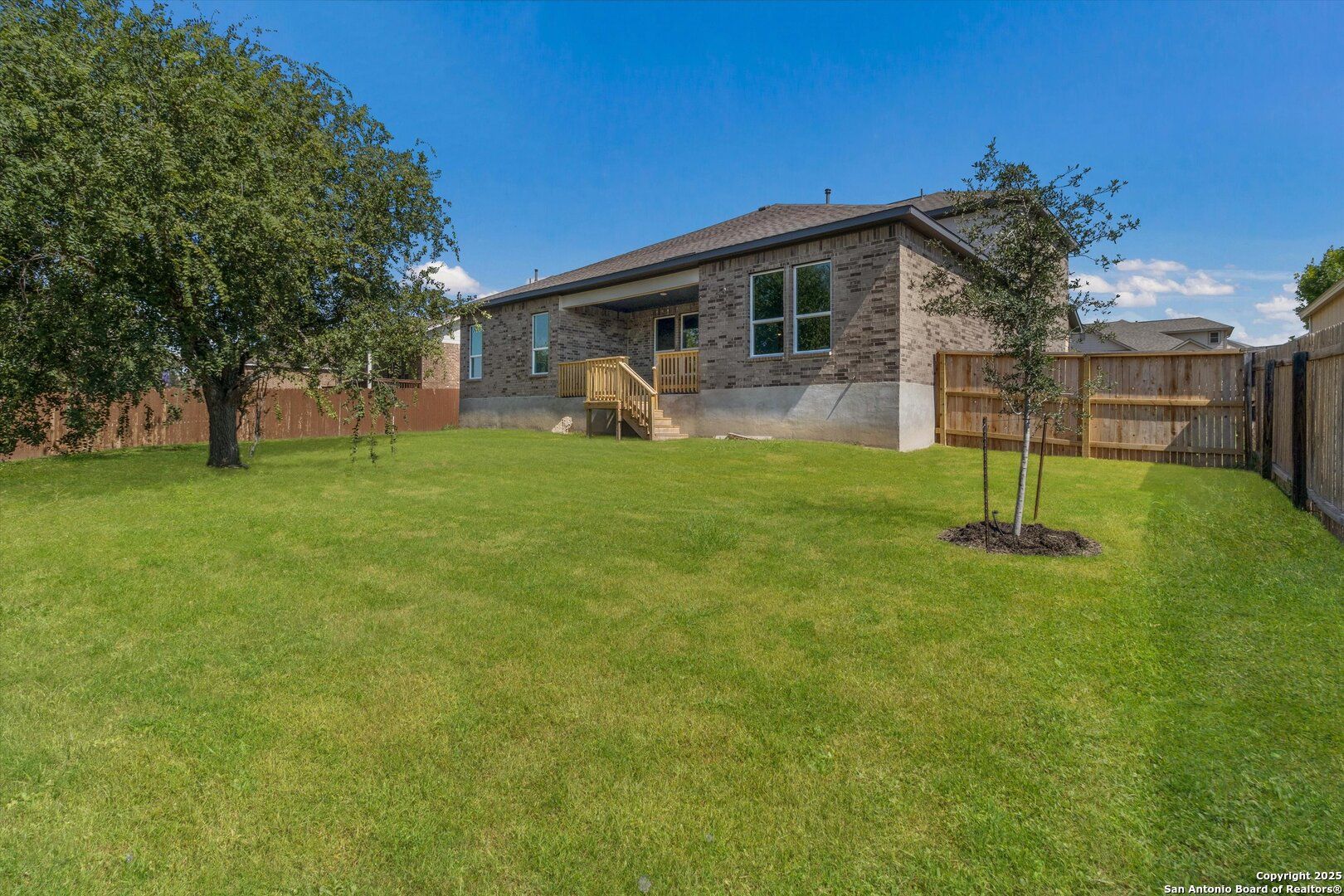 Backyard view of two-story brick home with covered patio, stairs, and lush green lawn in Ladera, San Antonio, Texas