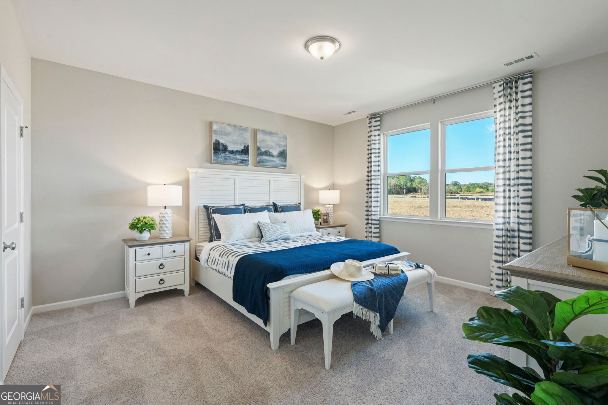 Serene master bedroom with white king bed, blue bedding, lamps, and field-view windows in Evermore Homes The Phoenix, Perry, GA