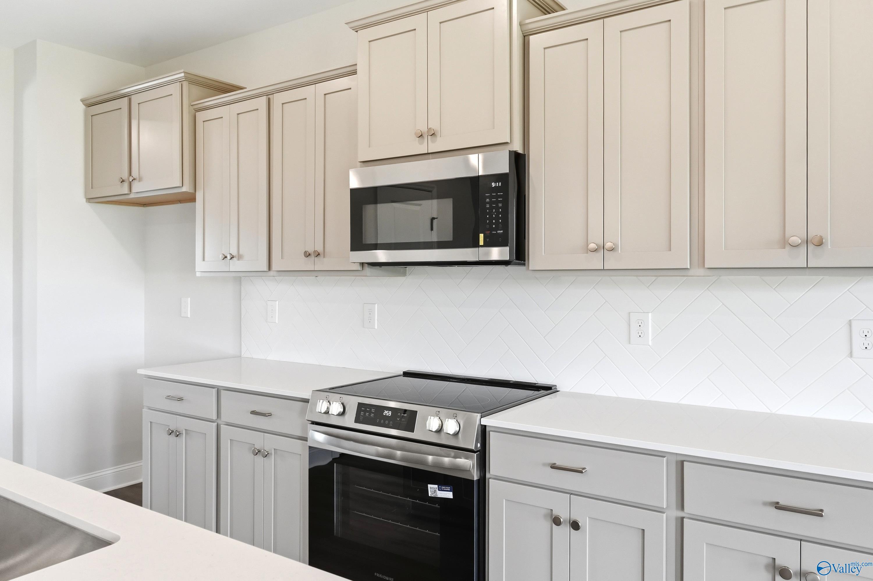 Modern kitchen with light gray cabinets, stainless steel appliances, and white herringbone tile in Davidson Homes Shelby A.