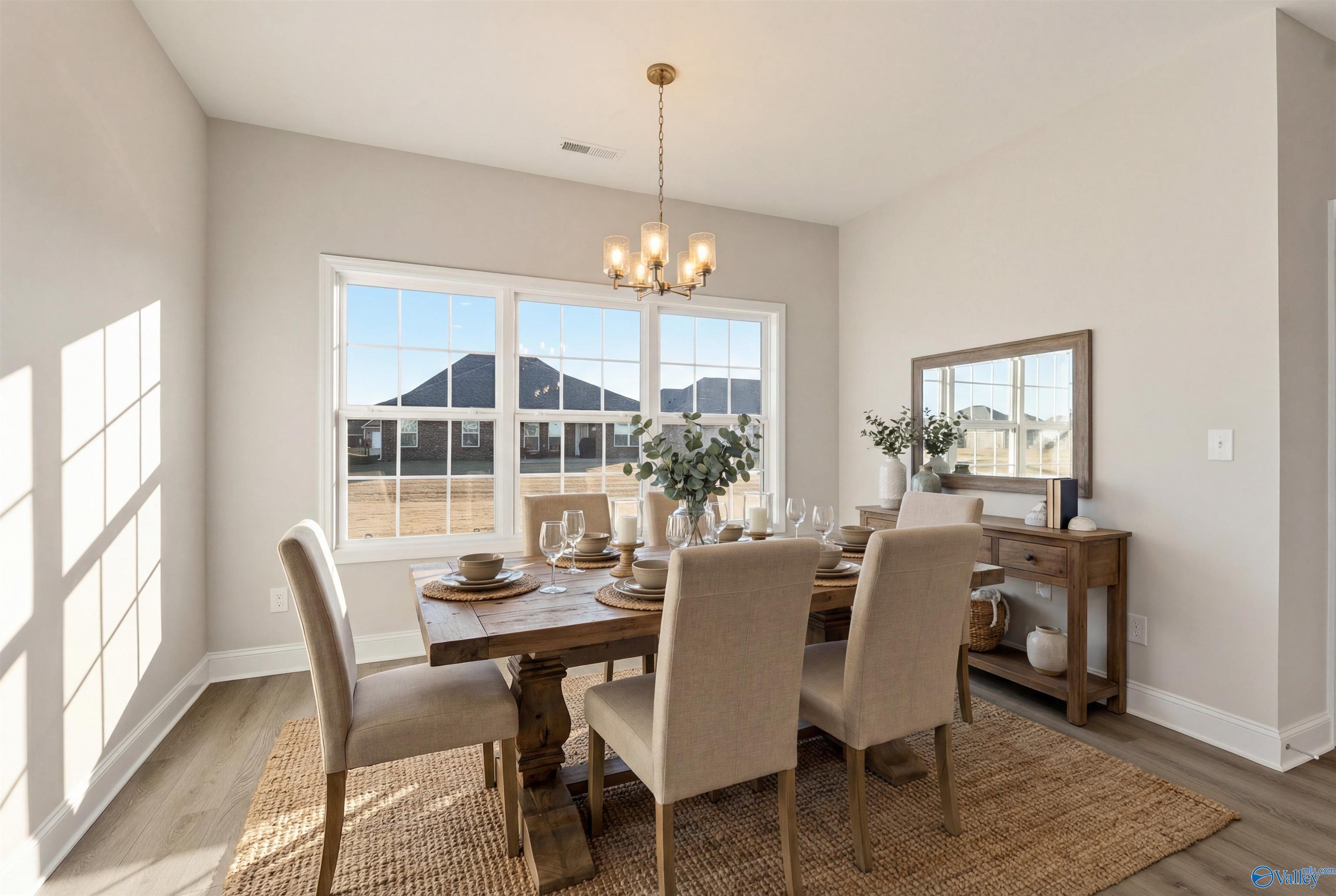 Bright dining room with farmhouse table, beige chairs, chandelier, and neighborhood view in The Montgomery B by Davidson Homes, Toney, Alabama