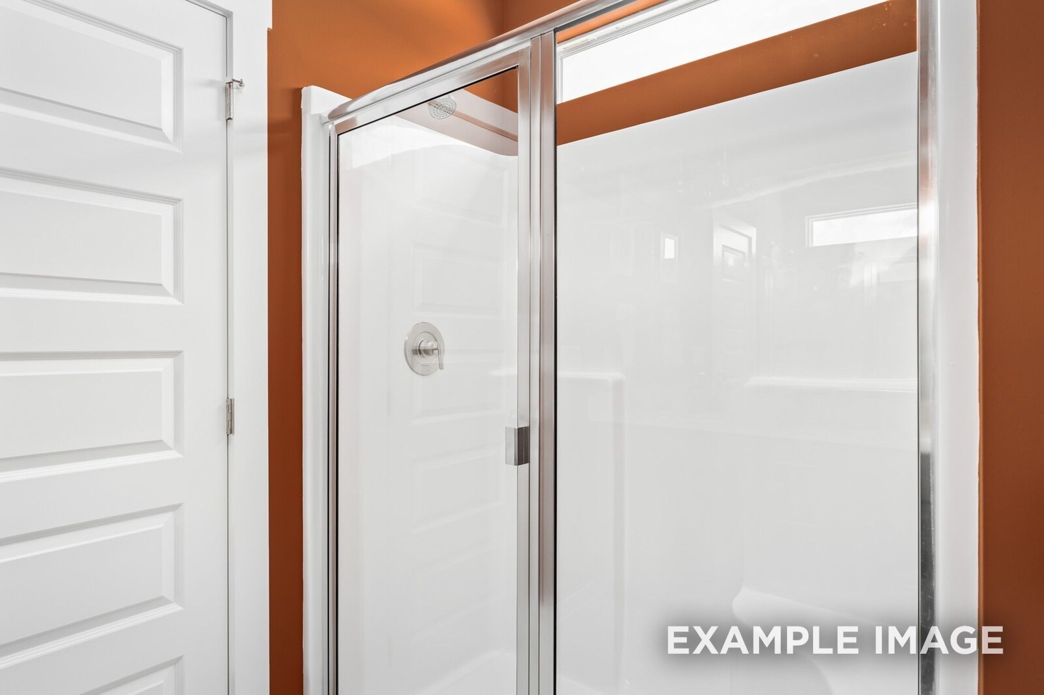 Modern glass shower enclosure with white tiles and orange accent wall in Davidson Homes The Ash A bathroom, Gallatin, TN