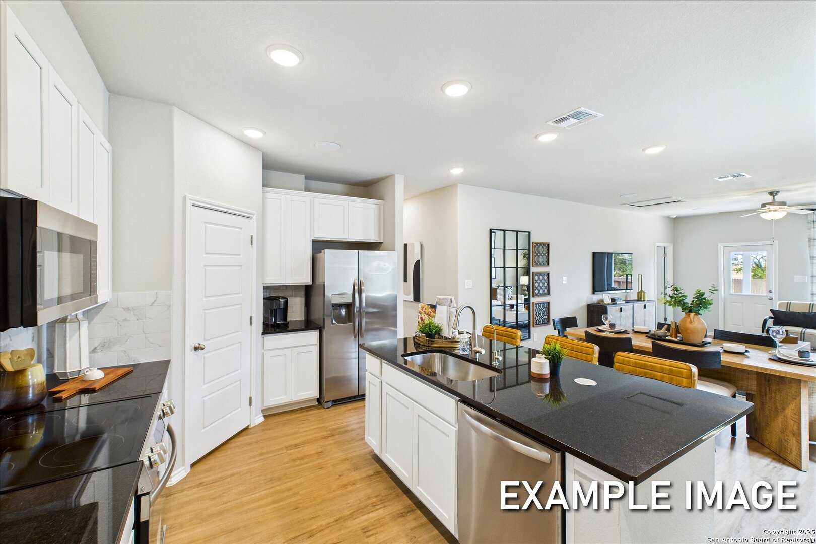 Modern open-concept kitchen with white cabinets, black granite island, stainless appliances in 4-bed Davidson Homes Sabine C, San Antonio