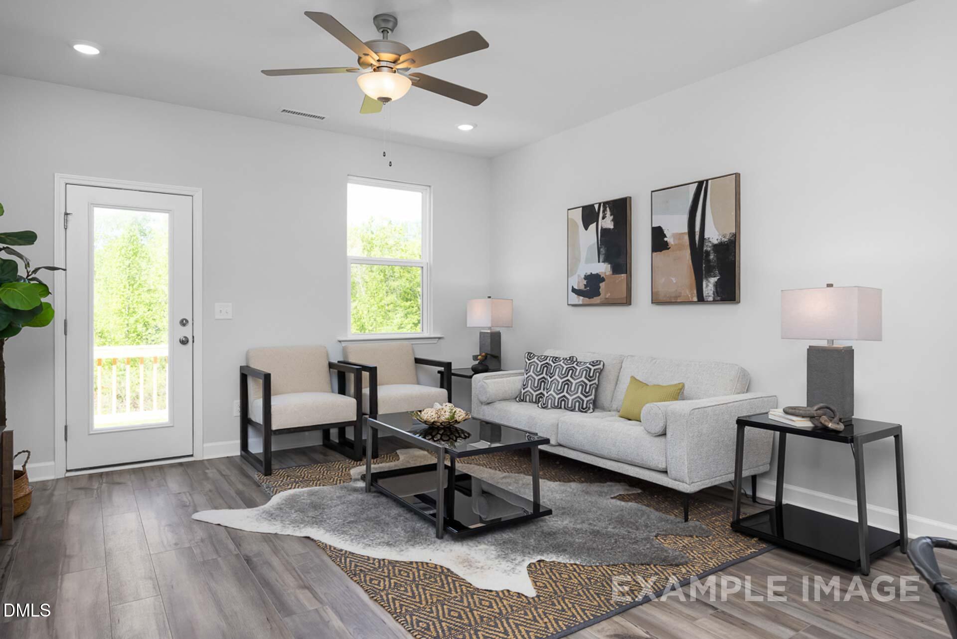 Modern living room with beige sofa, glass coffee table, abstract art, ceiling fan, and sliding door to patio in Davidson Homes The Carter C, Lillington, NC