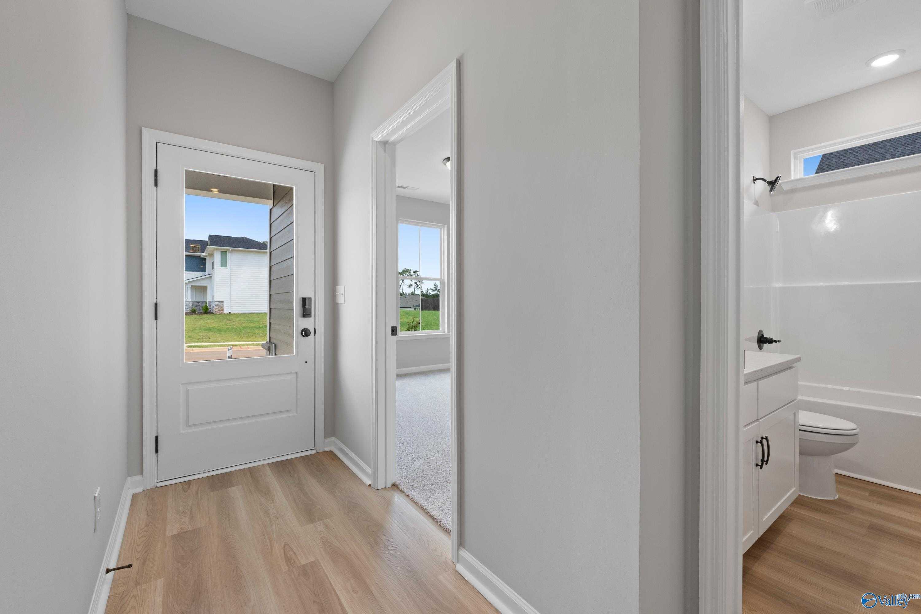 Bright hallway leading to modern bathroom with white vanity, tub, and window in The Nantucket 3-bedroom home, Madison, Alabama