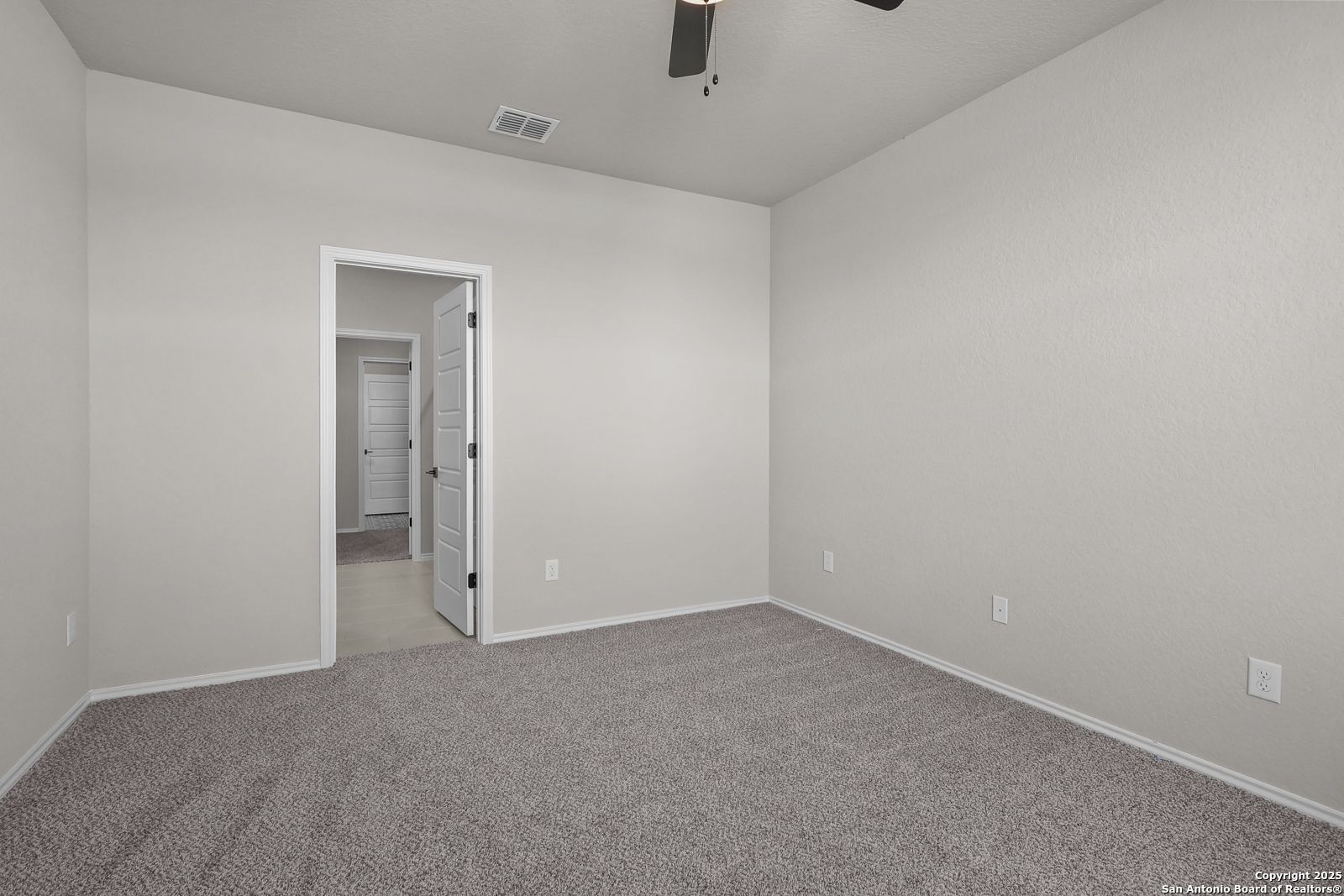 Spacious empty bedroom with ceiling fan, neutral beige walls, and carpet flooring in Davidson Homes The Brazos C, San Antonio