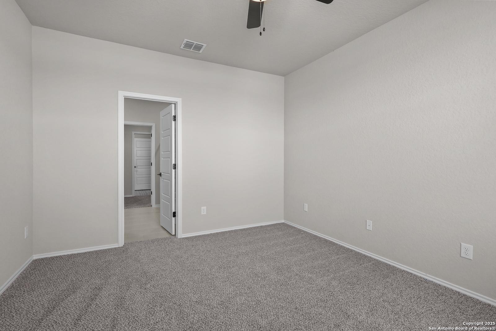 Spacious empty bedroom with ceiling fan, neutral beige walls, and carpet flooring in Davidson Homes The Brazos C, San Antonio