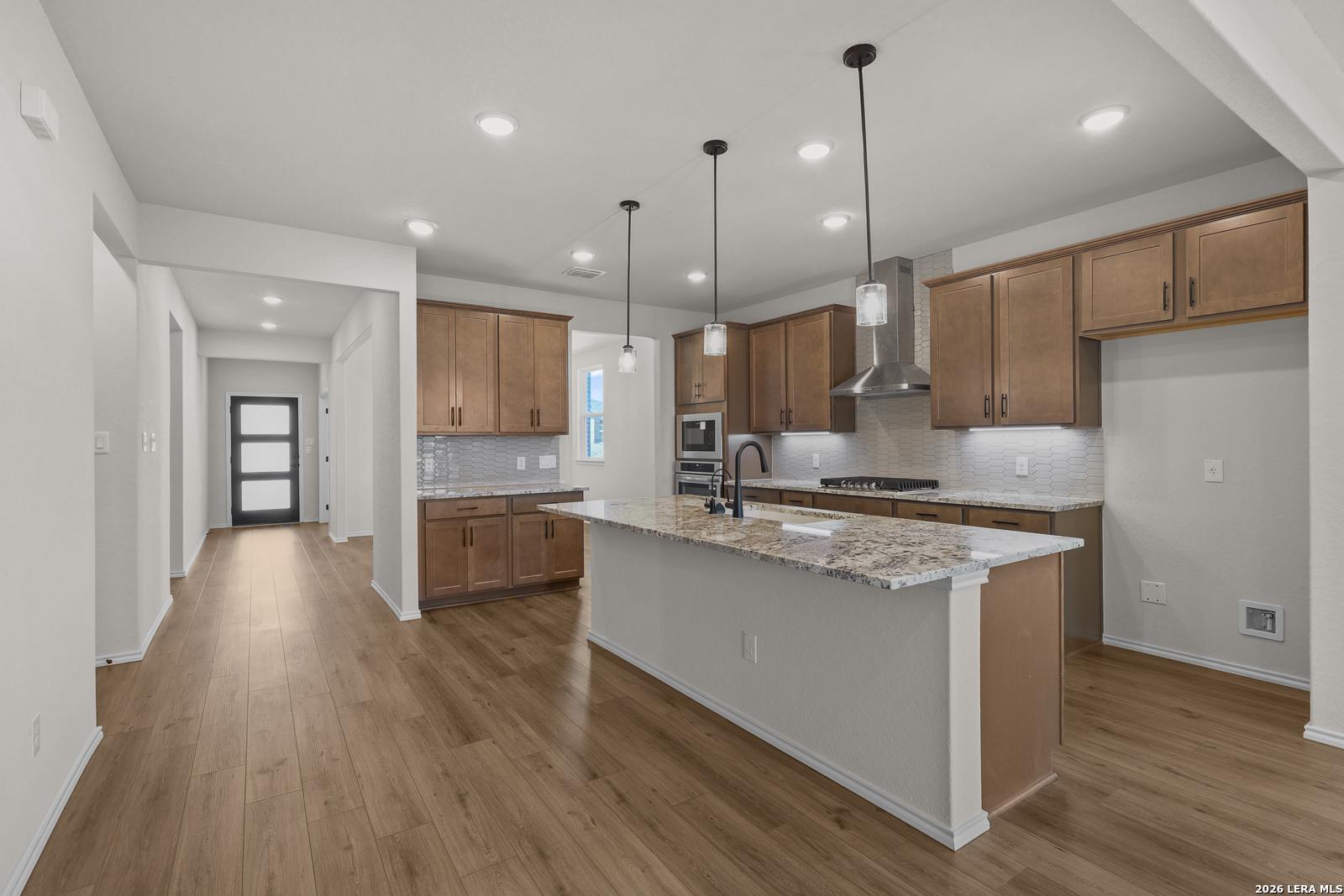 Open-concept kitchen with granite island, wood cabinets, and pendant lighting in Davidson Homes Glenwood E, Comanche Ridge, San Antonio