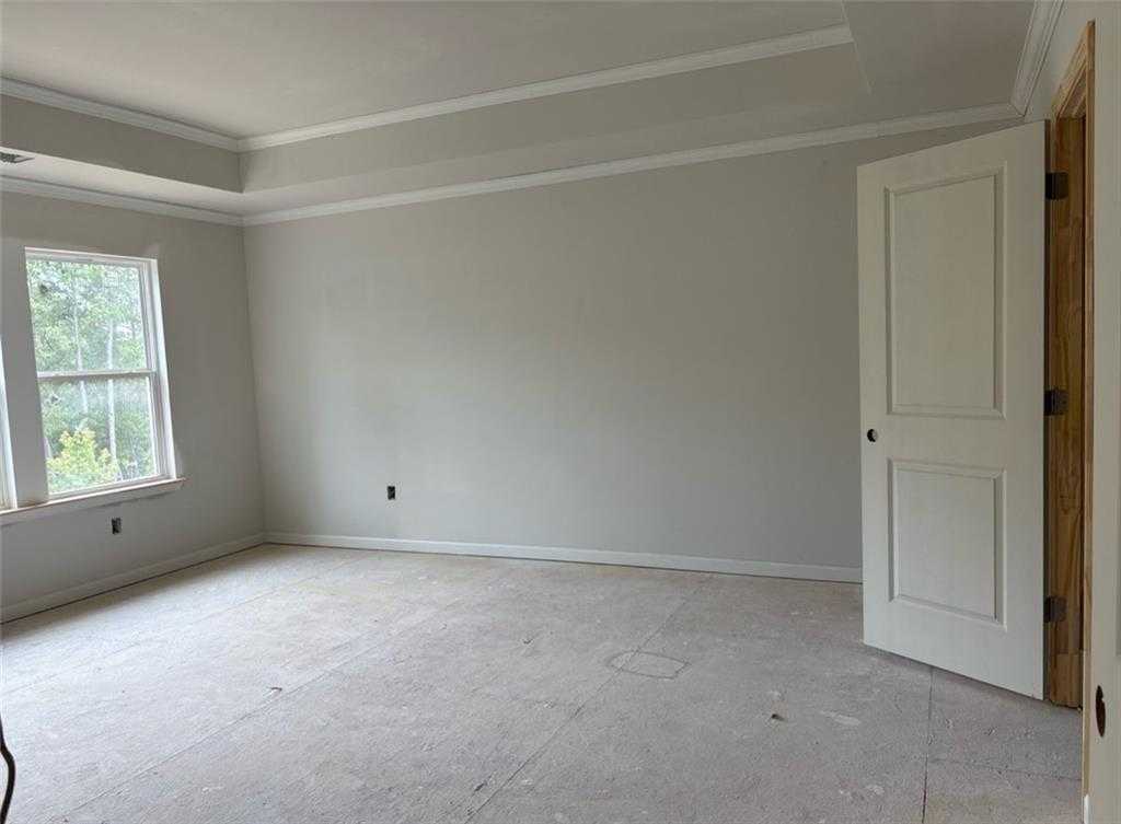 Unfinished bedroom featuring tray ceiling, light gray walls, large windows, open door, and subfloor in Davidson Homes The Hickory A, Riverwood, Dallas, Georgia