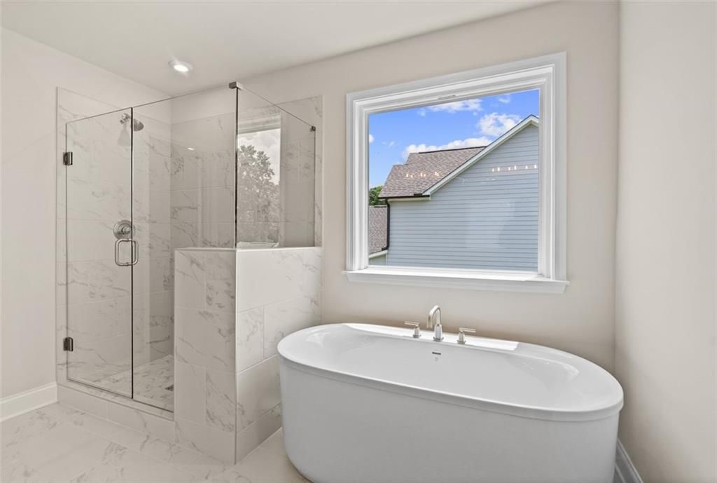 Luxurious master bathroom with frameless glass shower, freestanding tub, and backyard view in Davidson Homes The Hickory B at Wehunt Meadows, Hoschton