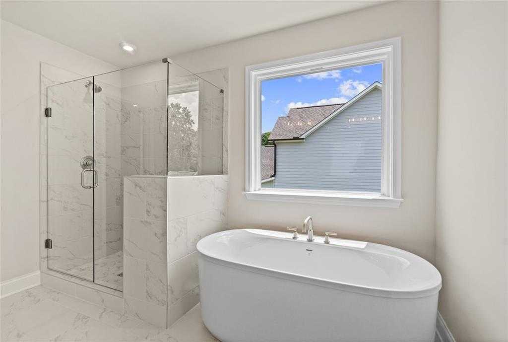 Luxurious master bathroom with frameless glass shower, freestanding tub, and backyard view in Davidson Homes The Hickory B at Wehunt Meadows, Hoschton