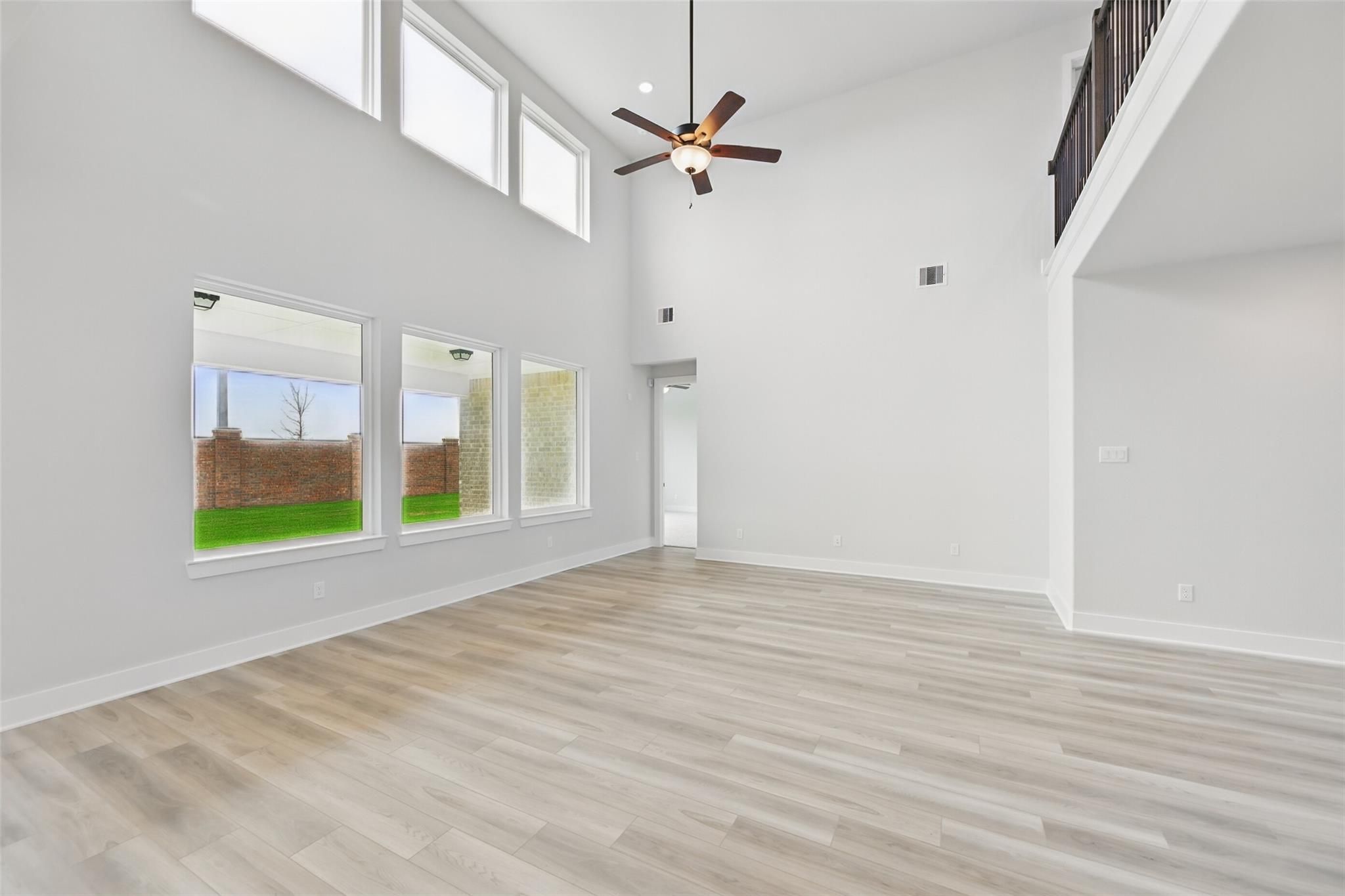 Spacious two-story foyer with vaulted ceilings, large windows overlooking green yard, upstairs balcony, and ceiling fans in Davidson Homes The Victoria C, Lago Mar, Texas City