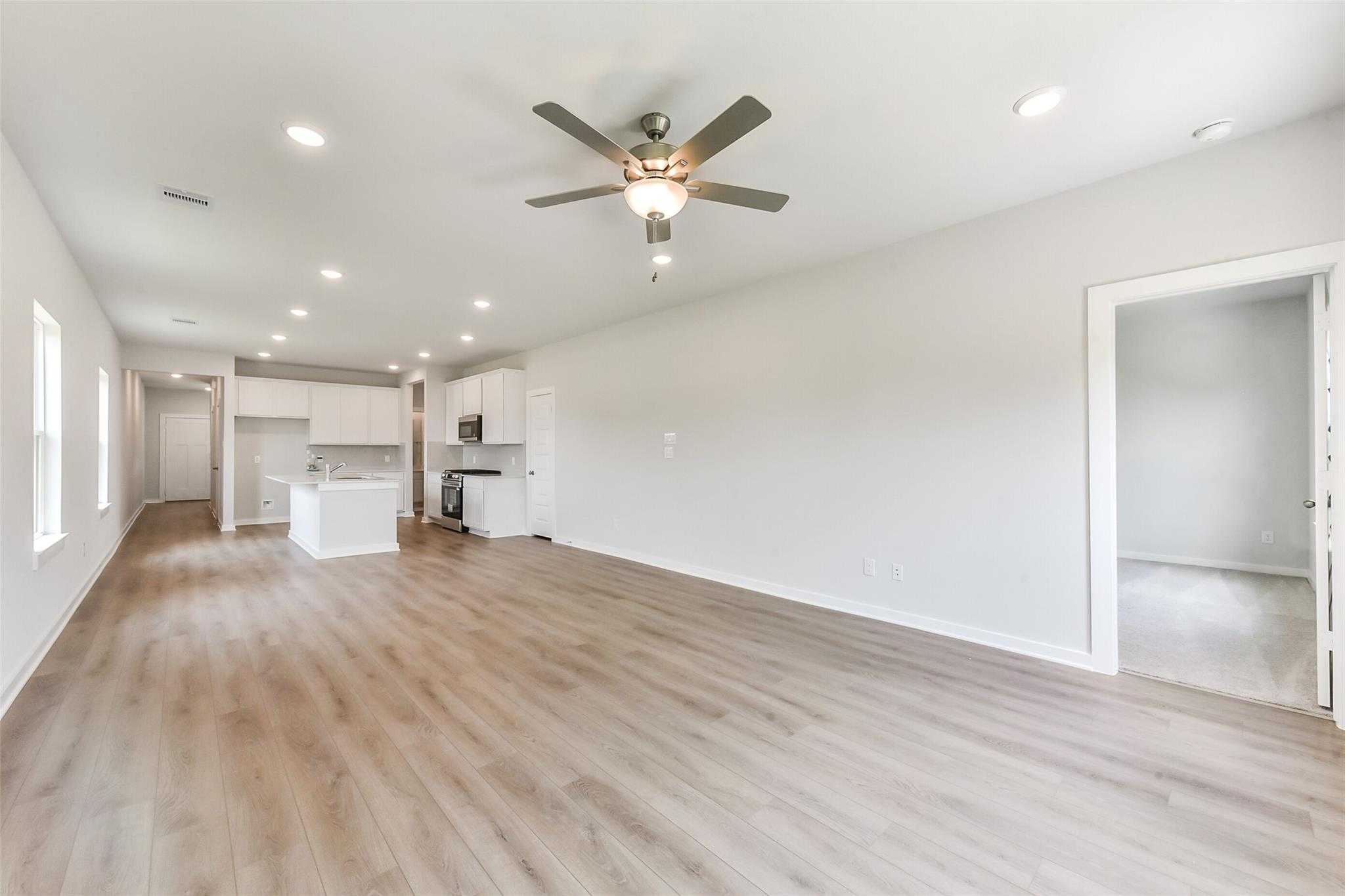 Open-concept kitchen and living room with white cabinets, ceiling fan, and luxury vinyl plank floors in Davidson Homes The Frio F, Dayton, Texas