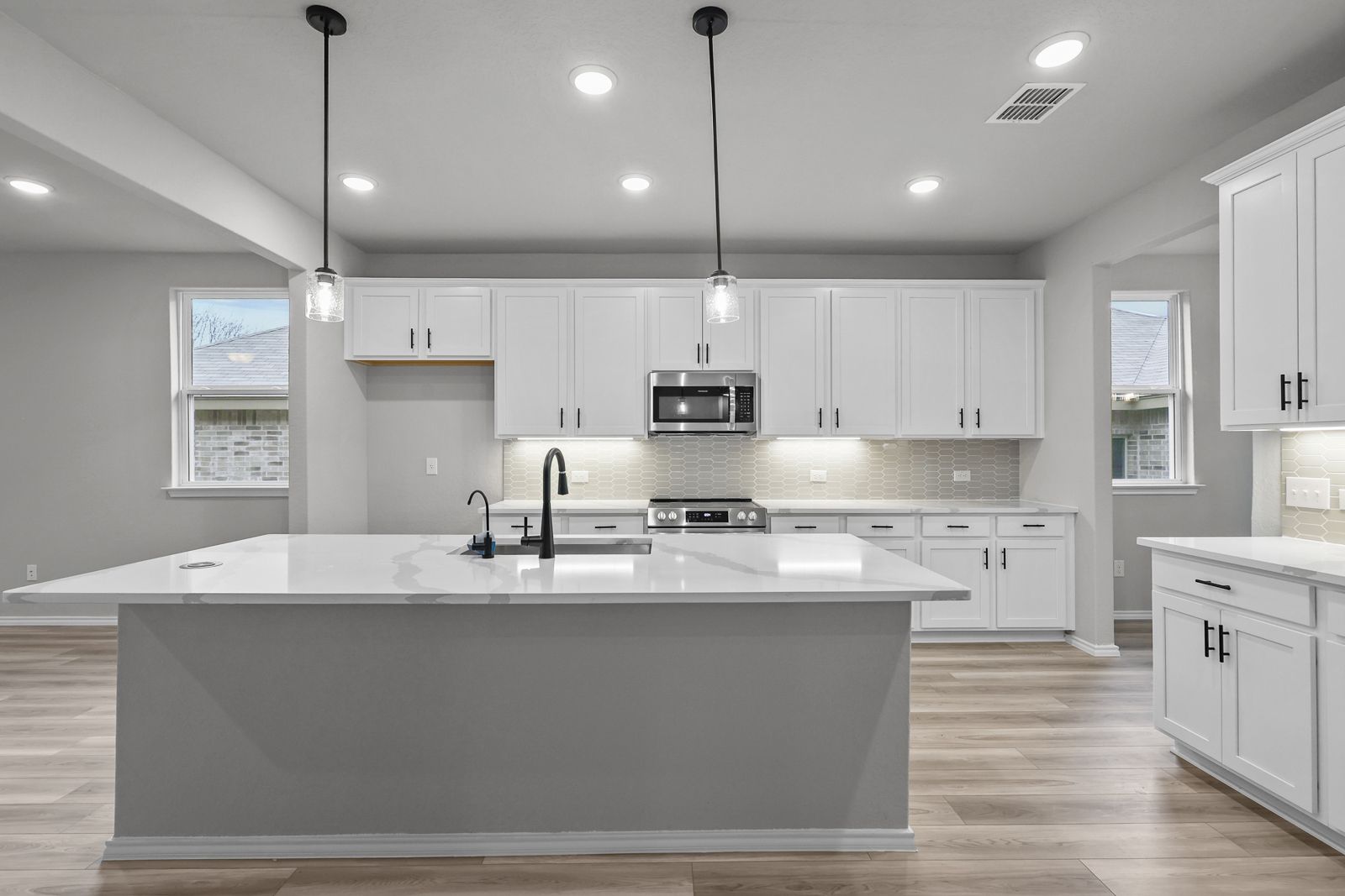 Modern kitchen in The Glenwood E featuring a large quartz island, white cabinetry, and stainless steel appliances.