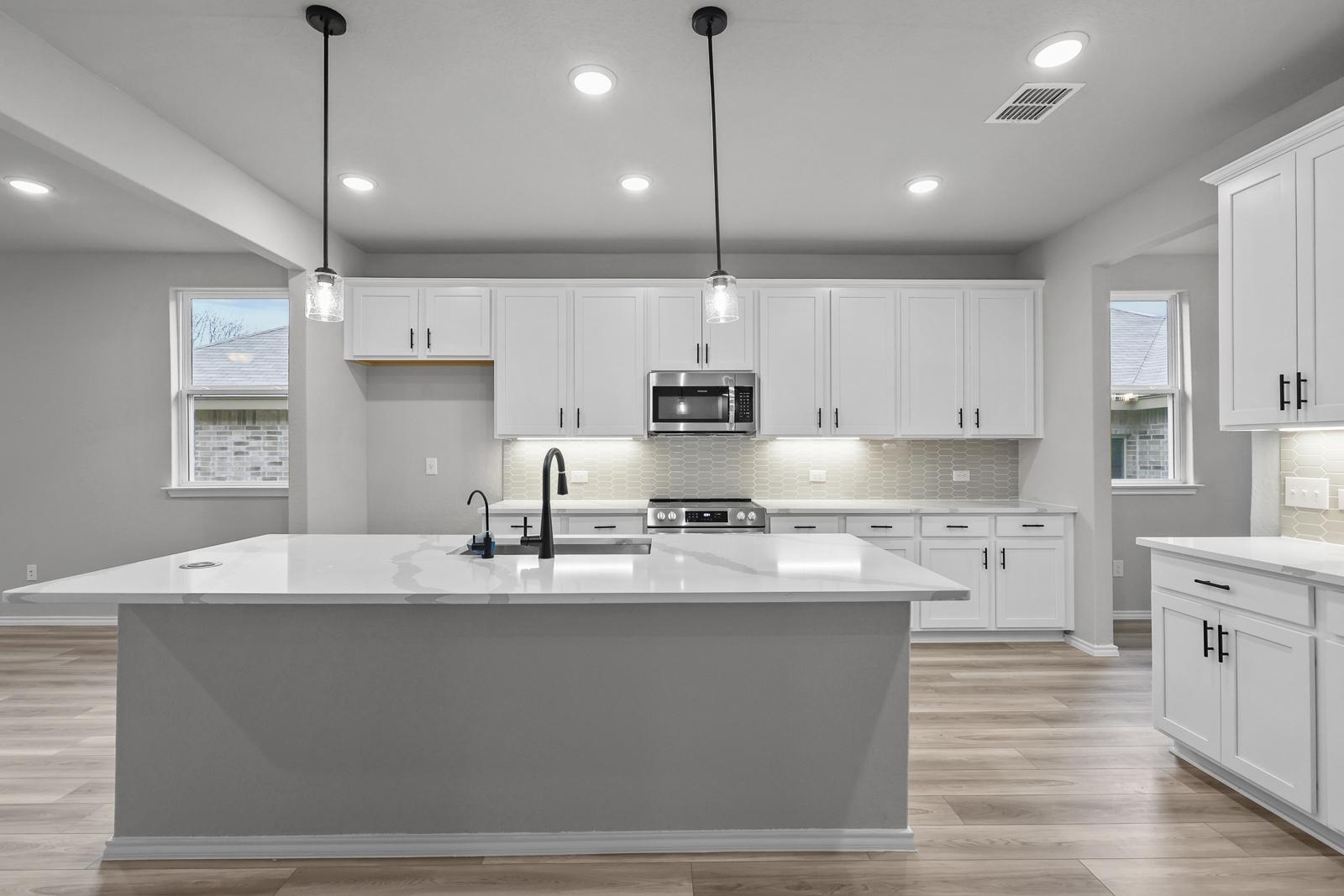 Modern kitchen in The Glenwood E featuring a large quartz island, white cabinetry, and stainless steel appliances.
