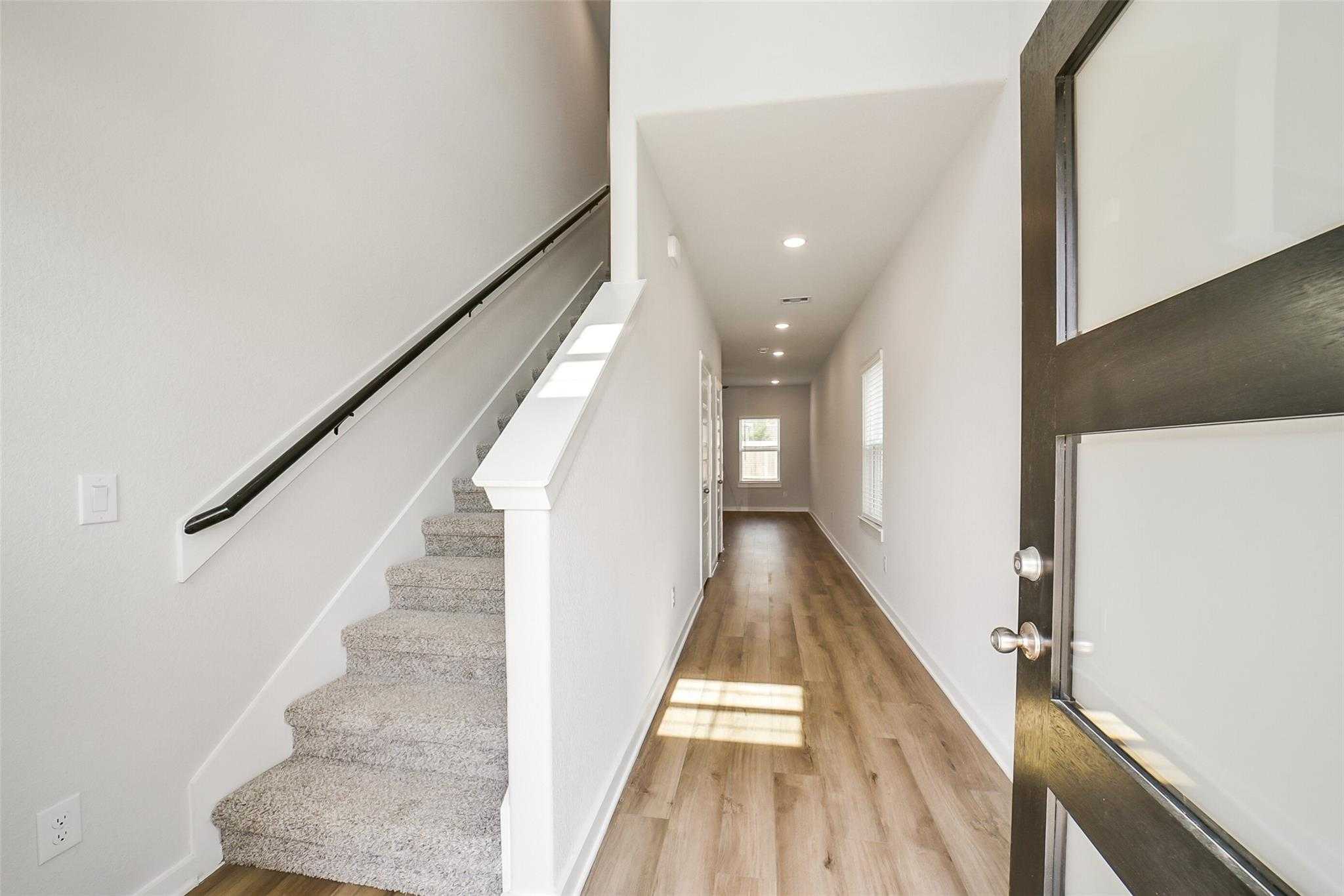 Bright entry hallway with carpeted staircase, white railings, hardwood floors, and frosted glass door in Davidson Homes The Trinity F, Magnolia Texas