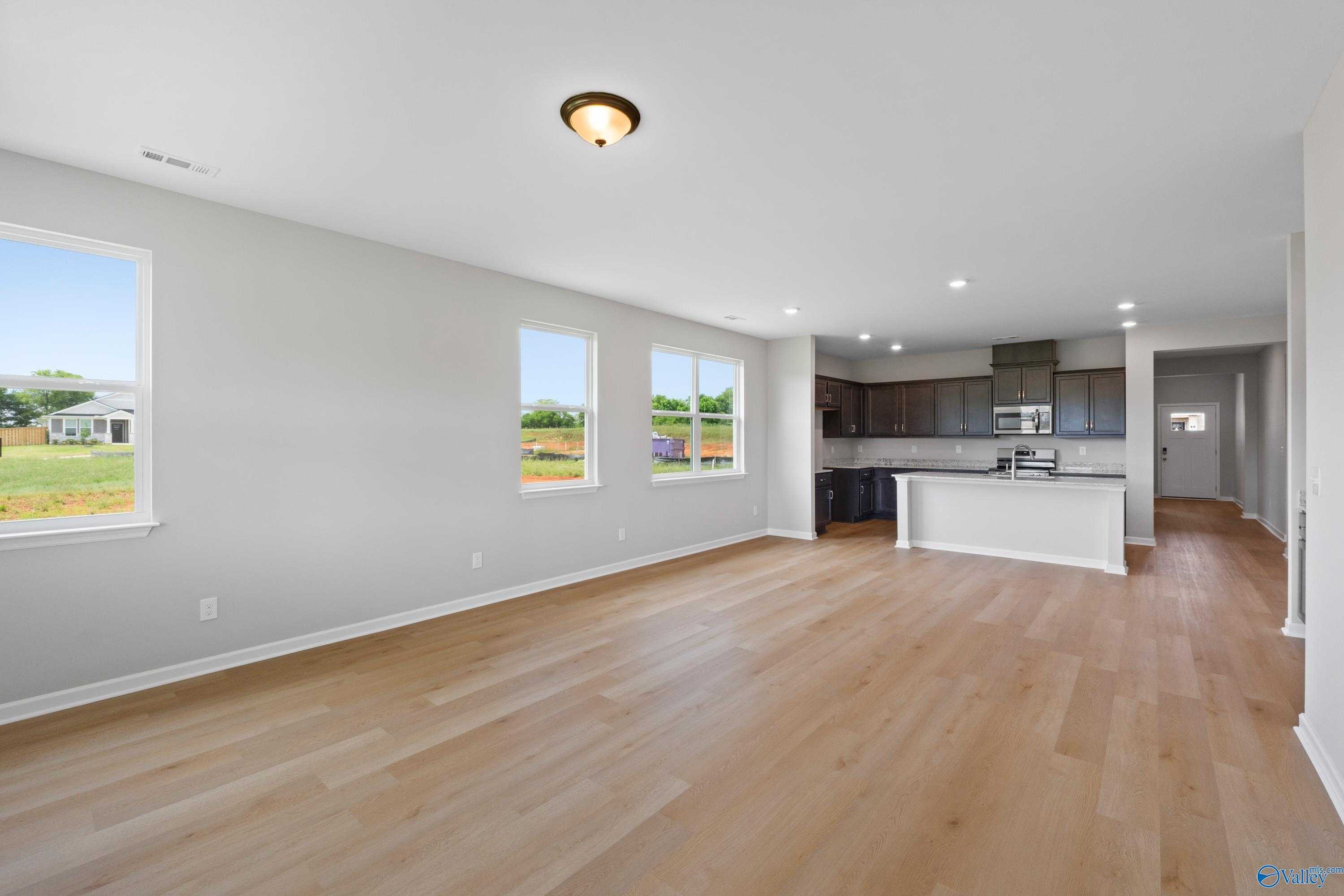 Open-concept living and kitchen with hardwood floors, large windows, and stainless appliances in The Aurora 4-bedroom home, Harvest, AL