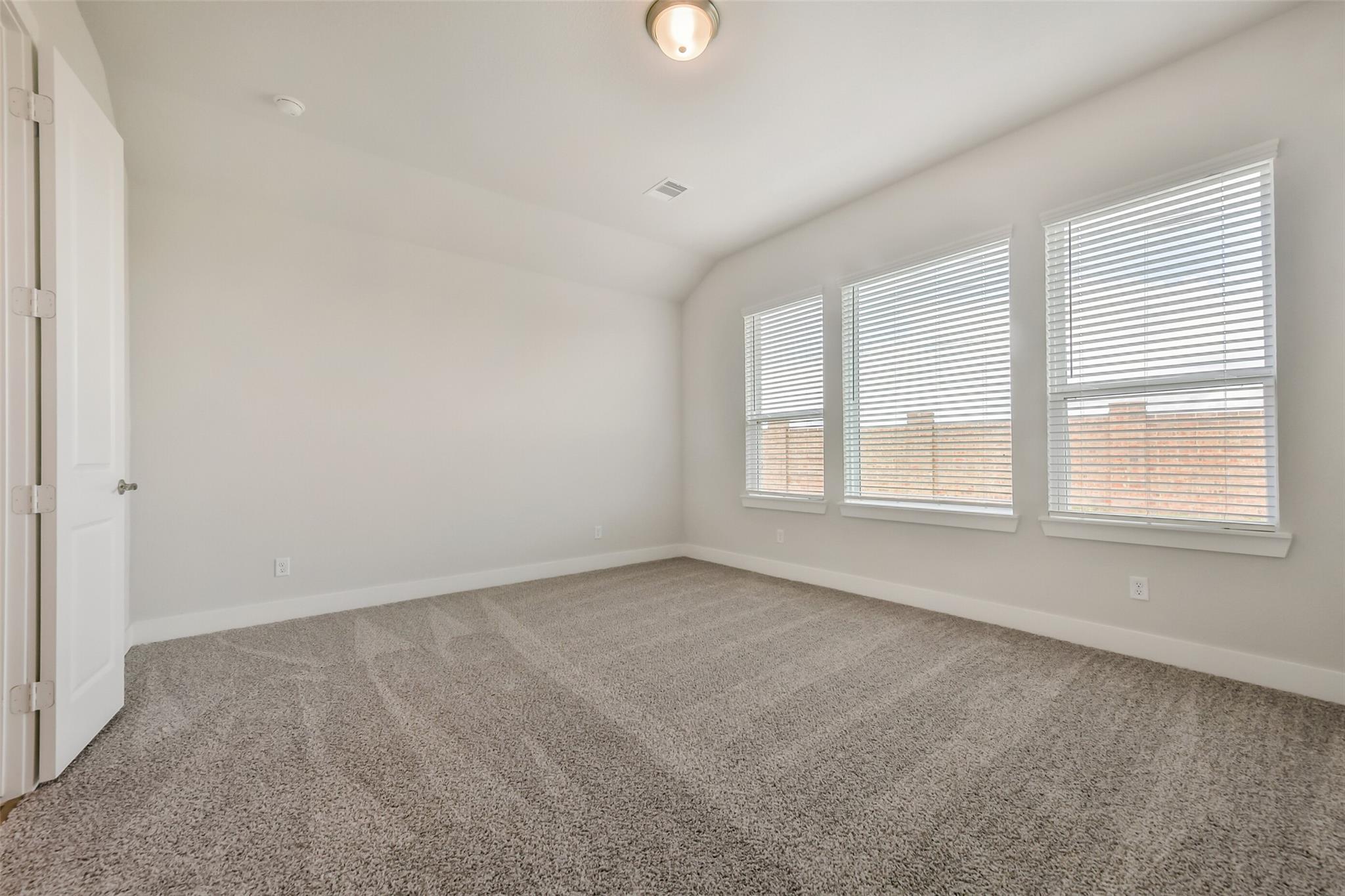 Spacious empty bedroom with beige carpet, white walls, large windows with blinds in Davidson Homes The Victoria A, Lago Mar, Texas City