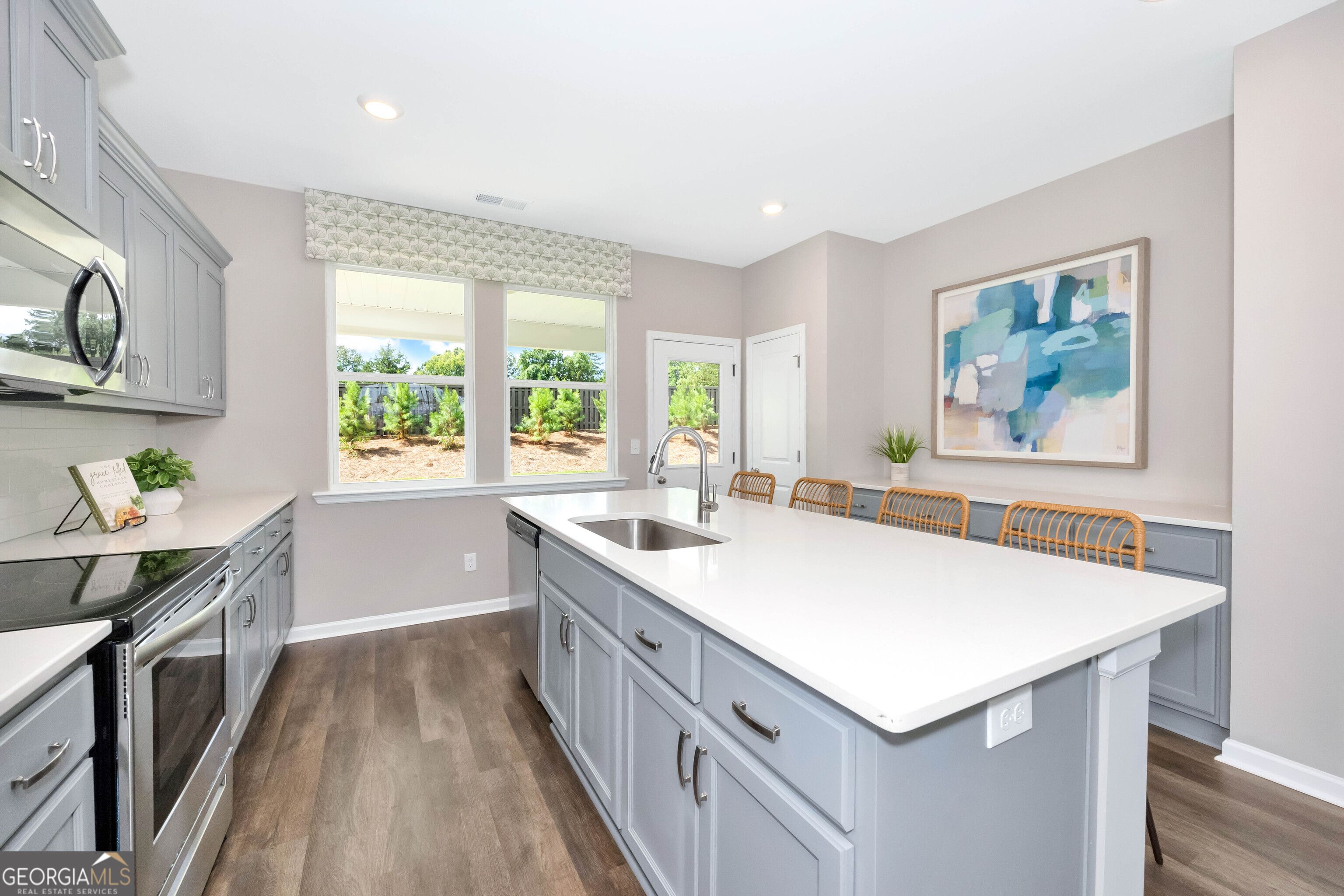 Modern open-concept kitchen with gray cabinets, white quartz island, farmhouse sink, and large windows overlooking greenery in Evermore Homes The Stella, Perry, Georgia