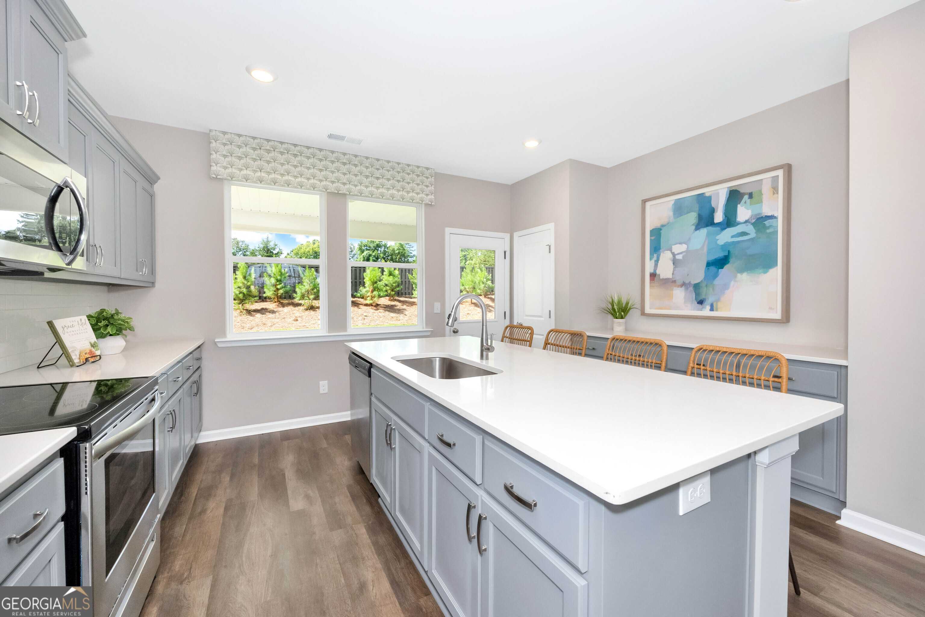 Modern open-concept kitchen with gray cabinets, white quartz island, farmhouse sink, and large windows overlooking greenery in Evermore Homes The Stella, Perry, Georgia