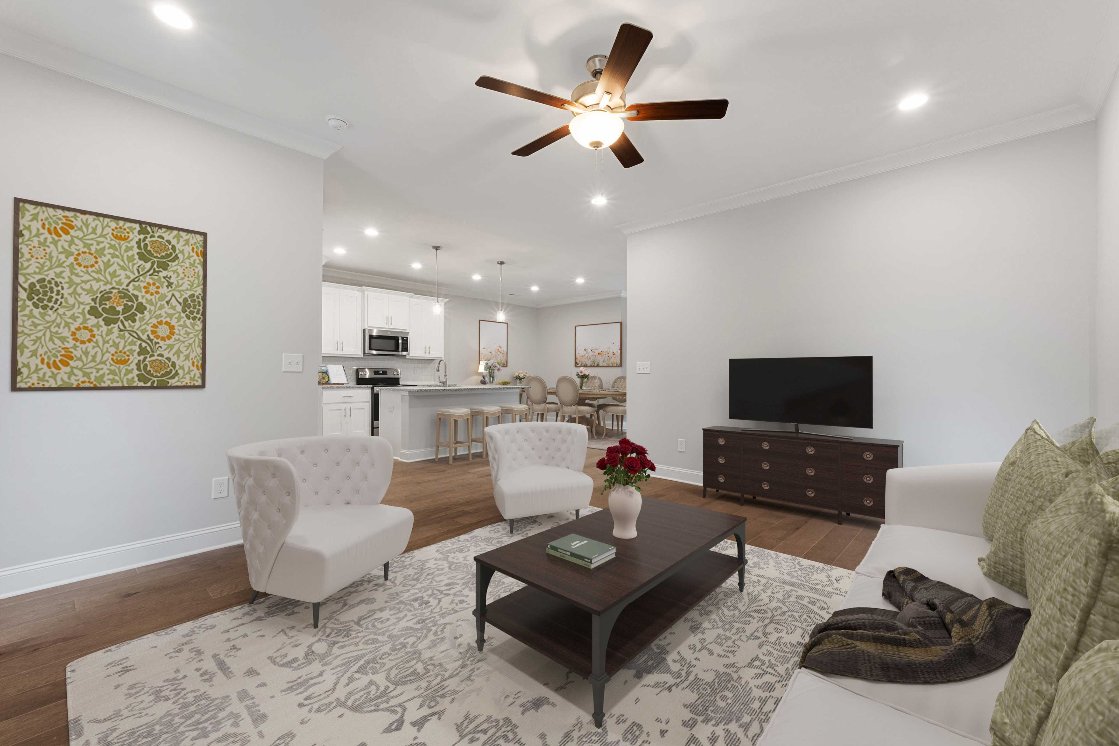 Open-concept living room in The Villas at Barnett's Crossing, Madison Alabama featuring hardwood floors, white armchairs, and open kitchen
