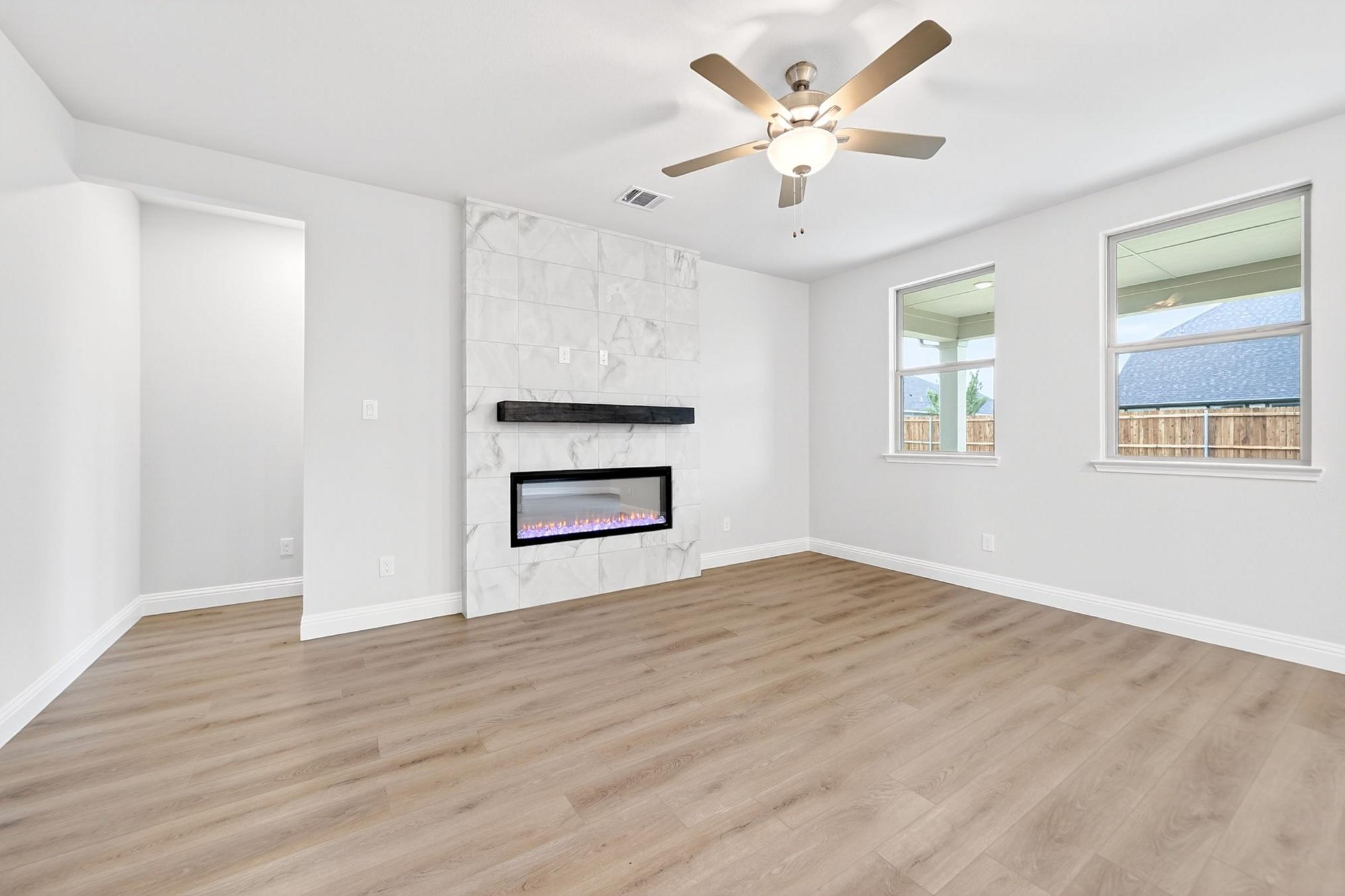 Bright living area in The Redbud featuring a modern marble fireplace, wood-look flooring, and a ceiling fan.