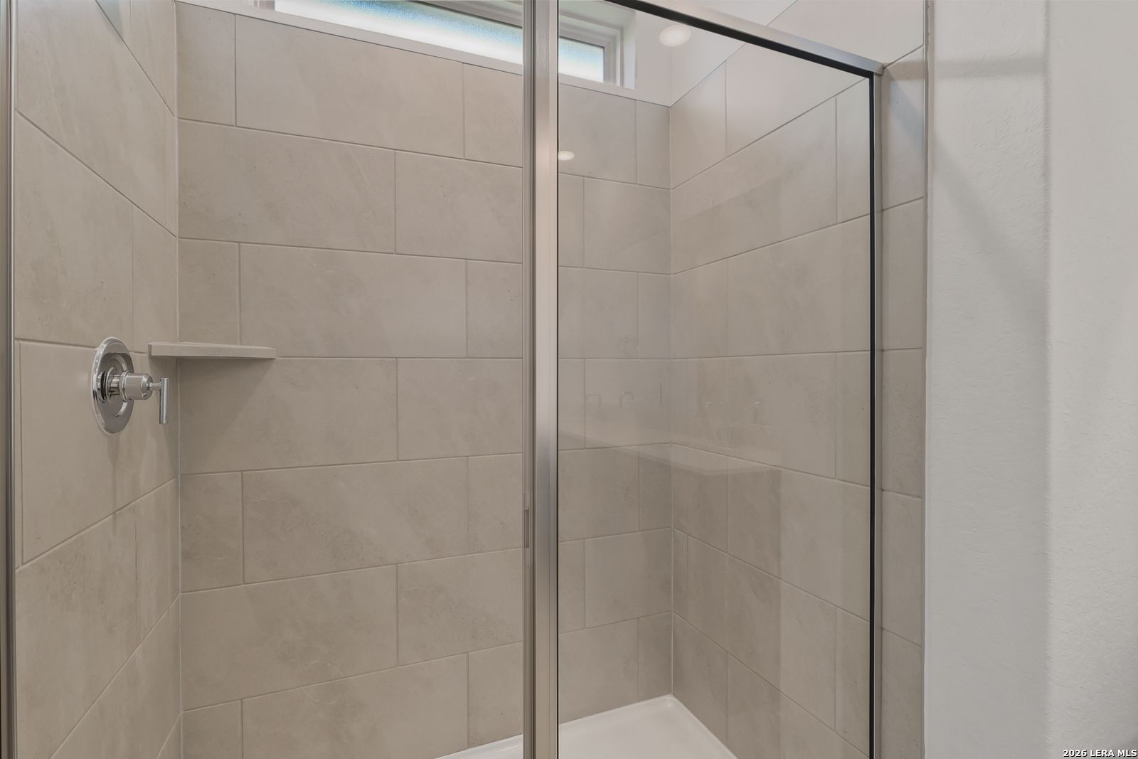 Modern walk-in shower with beige subway tiles, glass door, and chrome fixtures in master bathroom of Davidson Homes The Glenwood E, Elmendorf, Texas