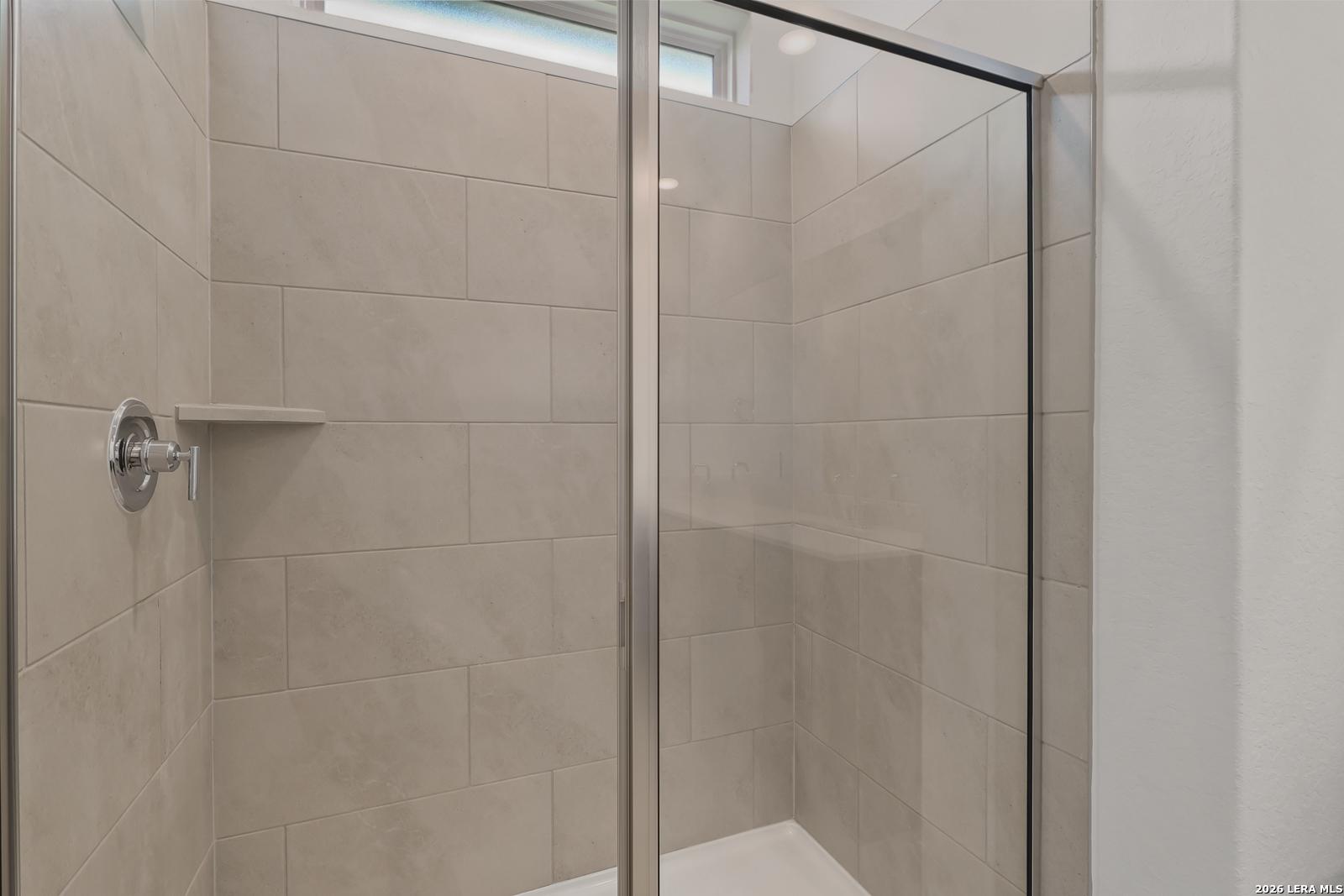 Modern walk-in shower with beige subway tiles, glass door, and chrome fixtures in master bathroom of Davidson Homes The Glenwood E, Elmendorf, Texas