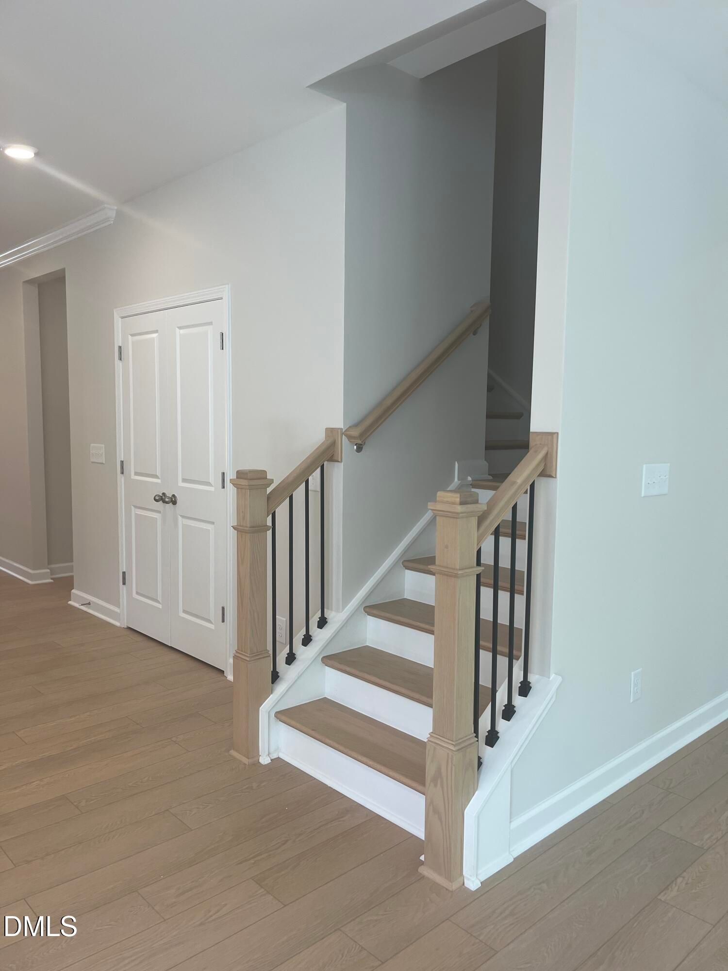Elegant oak staircase with black wrought iron balusters and adjacent white double doors in The Ashport L, Wake Forest, NC