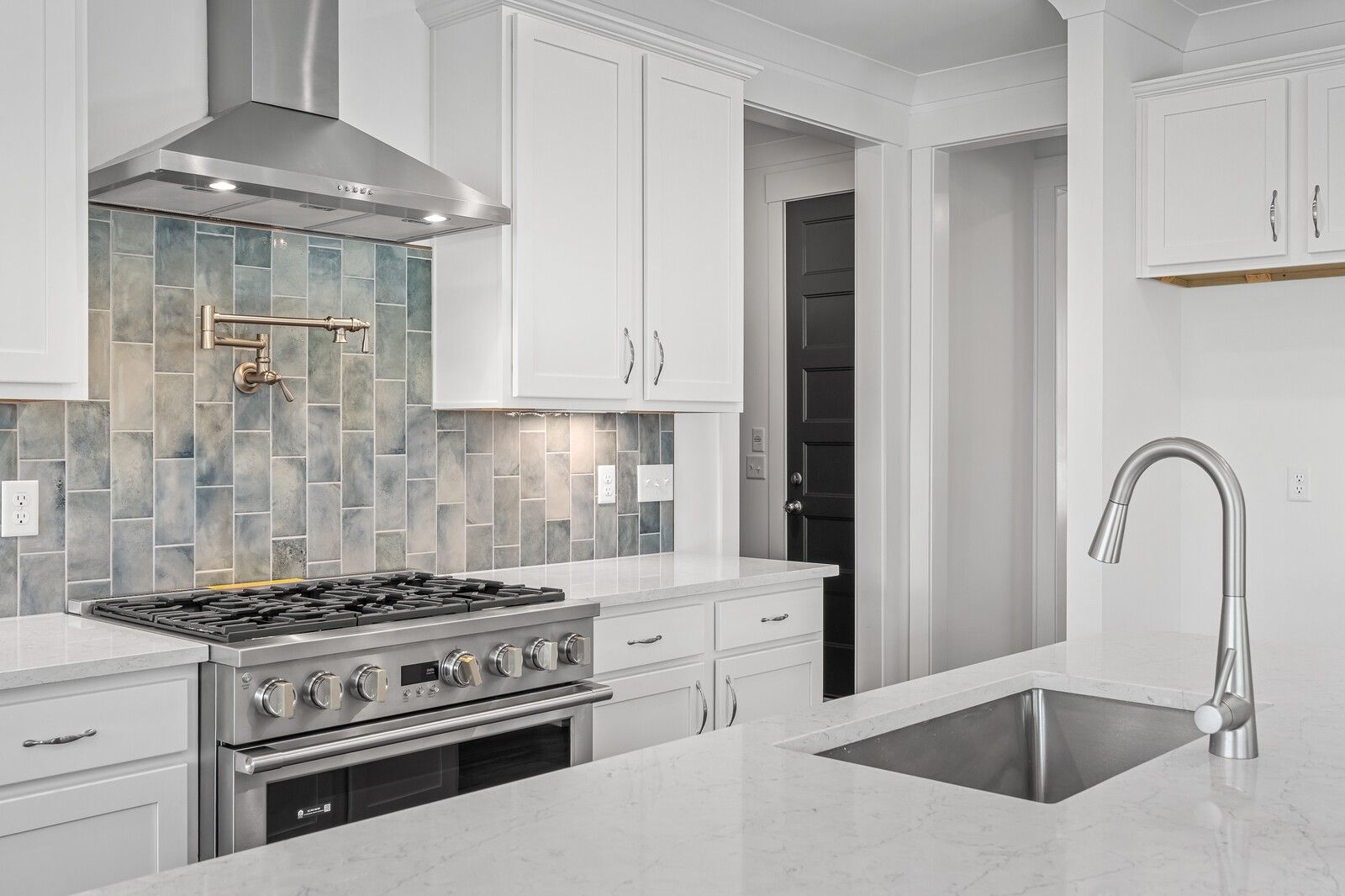 Modern kitchen featuring white cabinets, blue subway tile backsplash, stainless steel gas range and island sink in The Hawkins by Davidson Homes, Murfreesboro