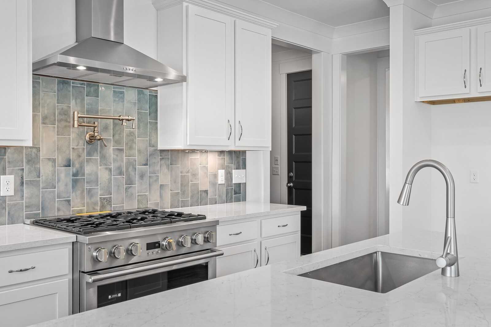 Modern kitchen featuring white cabinets, blue subway tile backsplash, stainless steel gas range and island sink in The Hawkins by Davidson Homes, Murfreesboro
