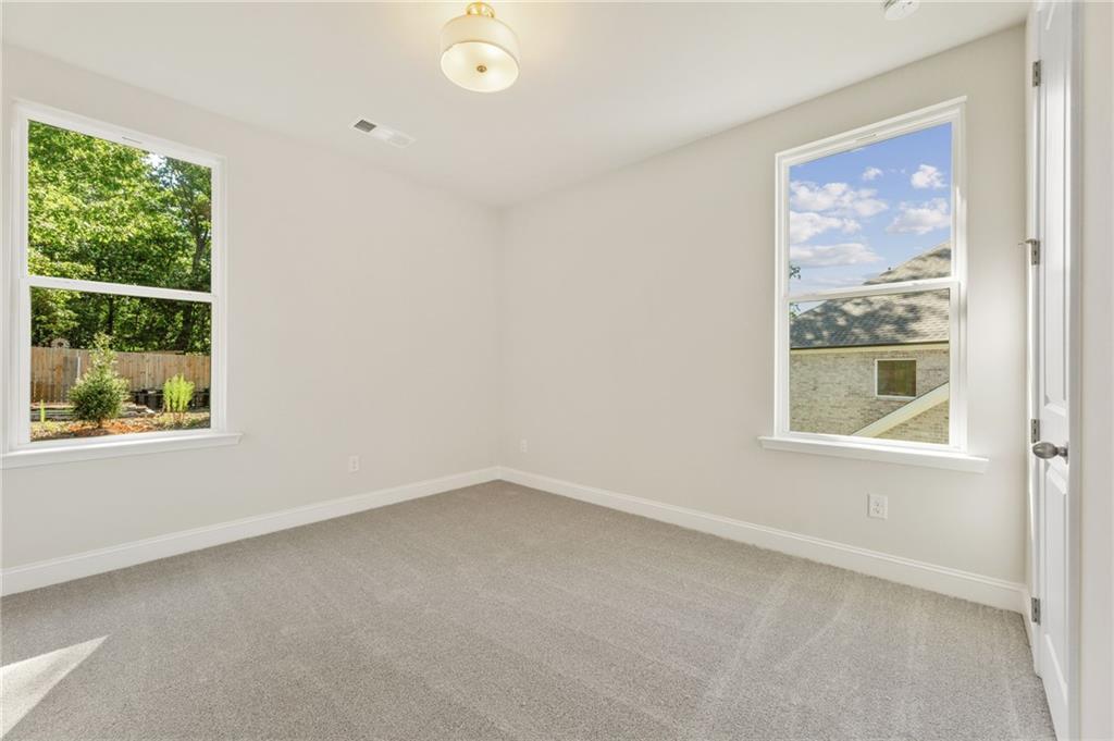 Bright empty bedroom with neutral walls, gray carpet, and large windows overlooking trees in Davidson Homes The Danbury E, Buford, GA