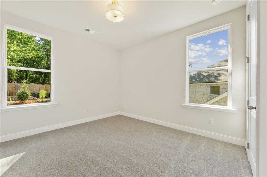 Bright empty bedroom with beige walls, gray carpet, large windows overlooking trees in Davidson Homes The Danbury E, Buford, GA