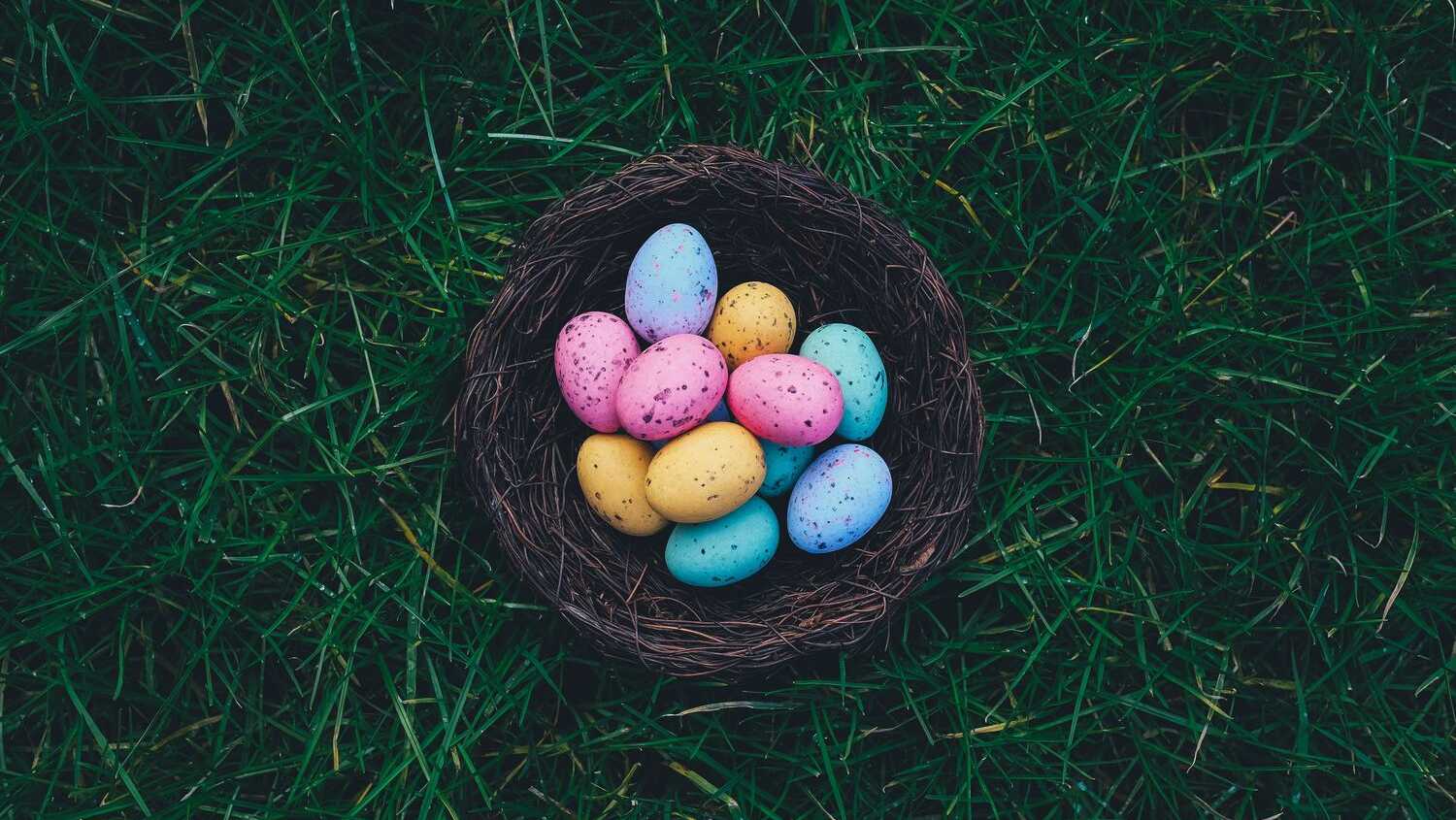Colorful pastel Easter eggs nestled in a woven basket on lush green grass