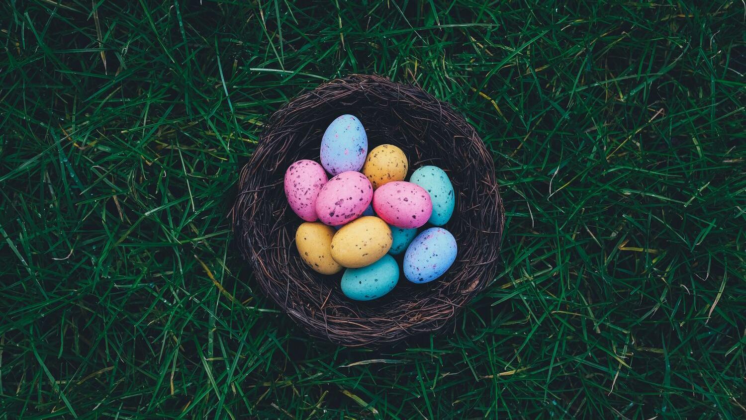Colorful pastel Easter eggs nestled in a woven basket on lush green grass