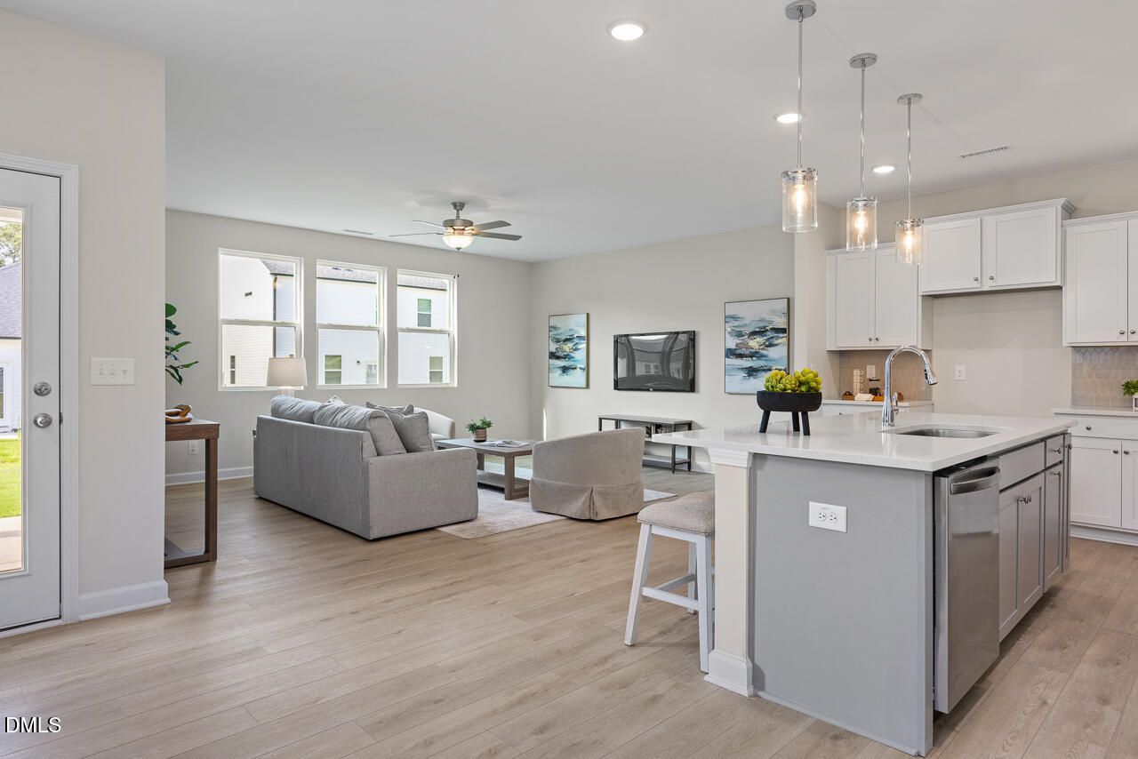 Open-concept living room with gray sofa and kitchen featuring white cabinets, gray island in Davidson Homes The Preston A, Lillington, NC